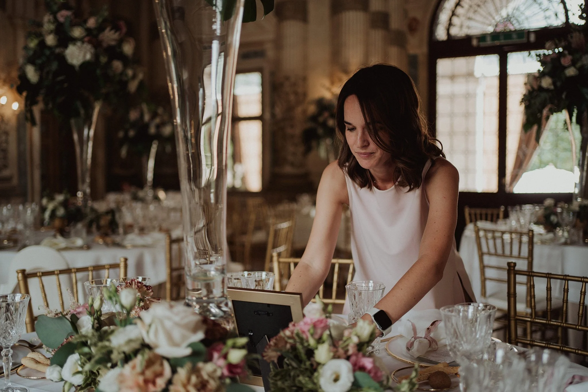 Una donna con capelli castani, allestisce il tavolo di un matrimonio elegante.
