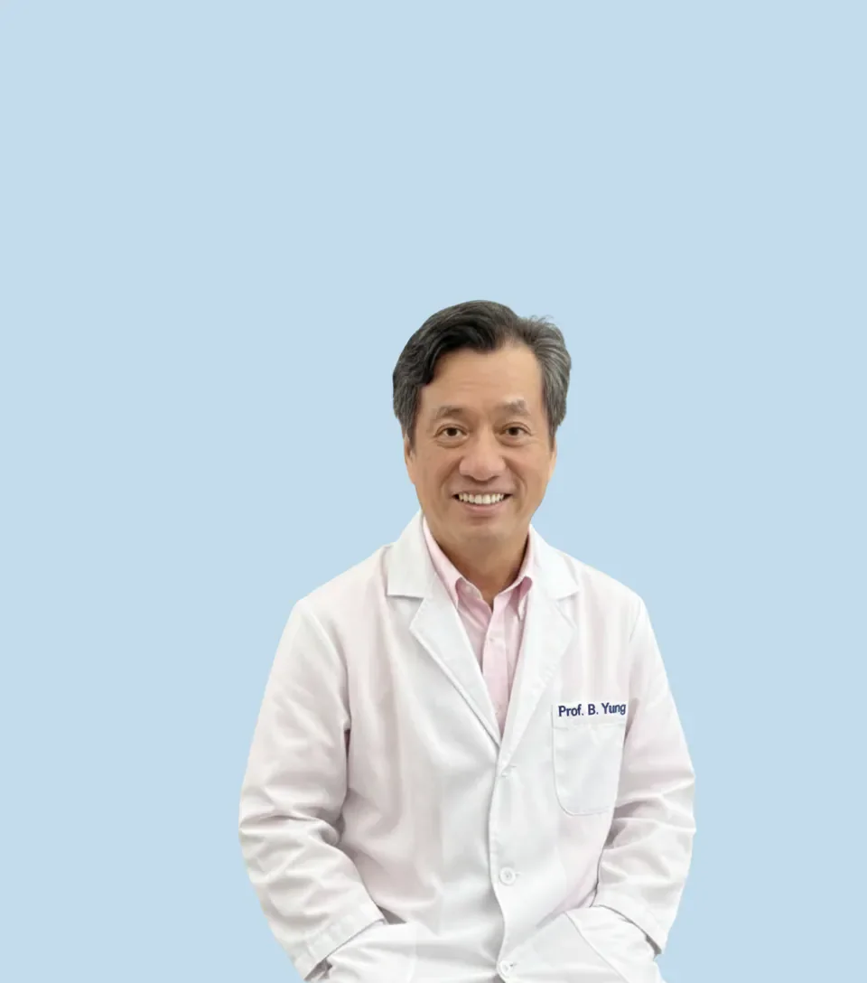 Professional portrait of a smiling male doctor wearing a white coat with the name tag 'Prof. B. Yung', standing against a plain light blue background.