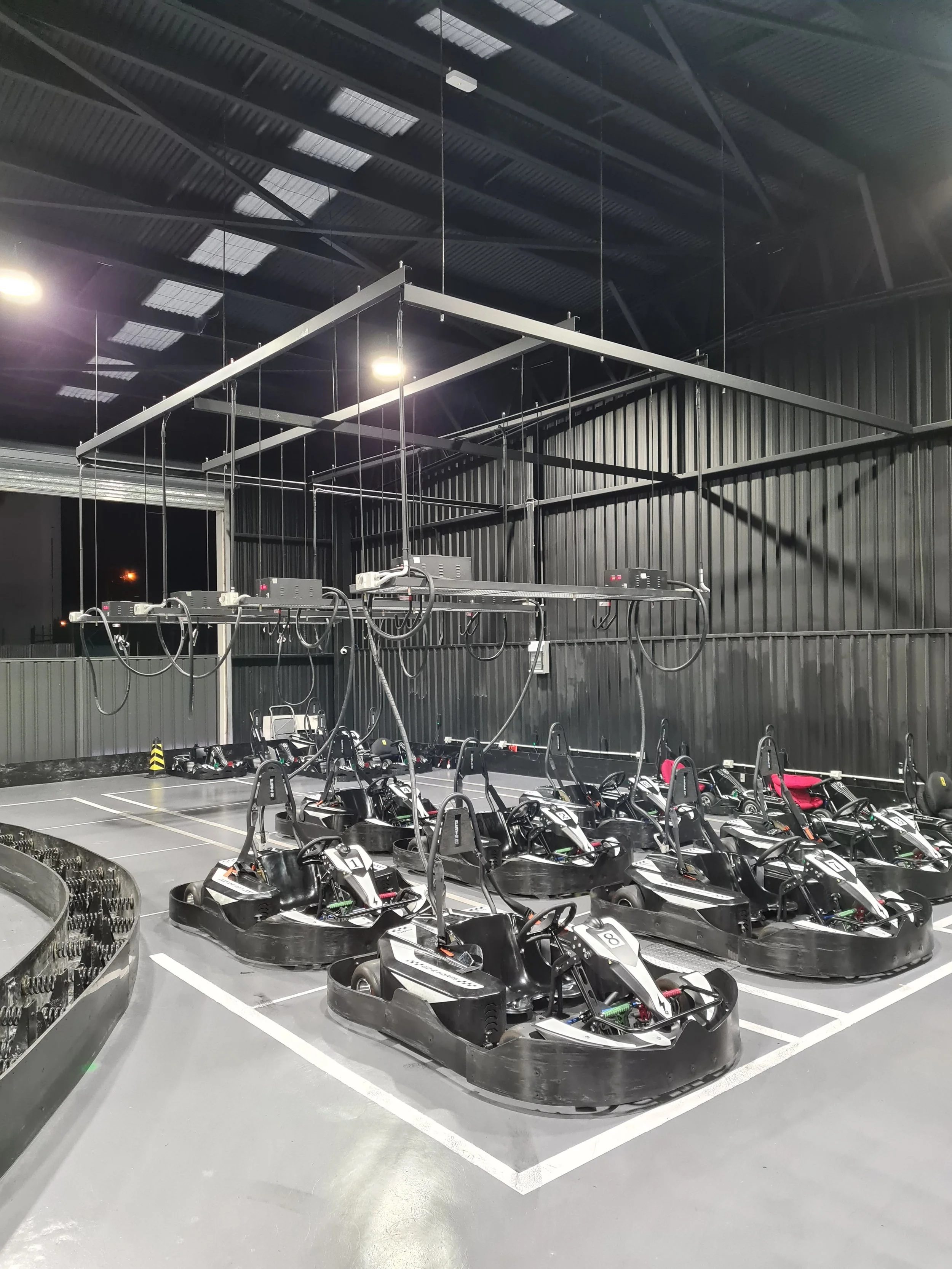 Indoor go-kart racing track with go-karts lined up in their lanes and a black metal wall in the background.