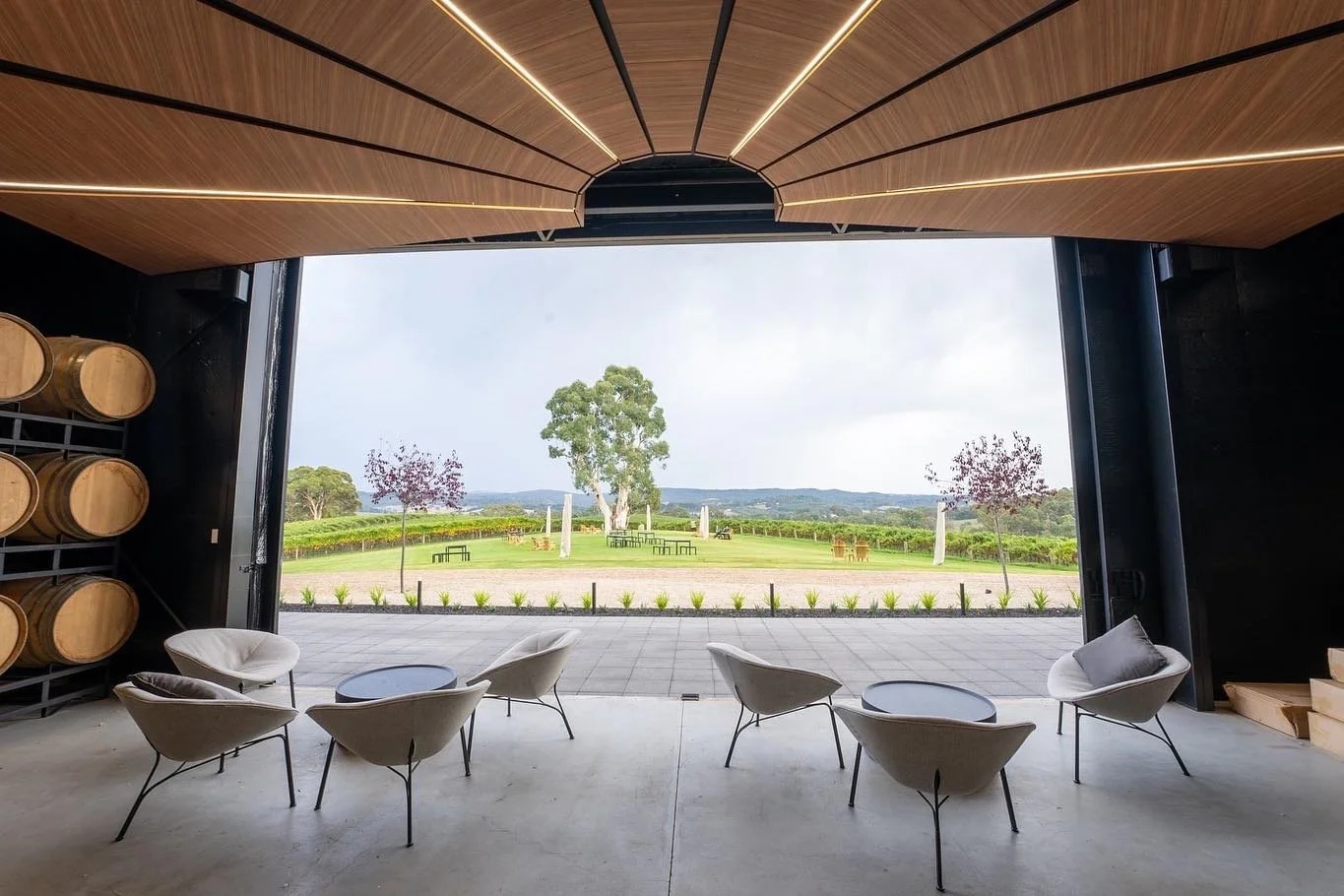 Modern indoor lounge area with large open doorway overlooking a scenic outdoor landscape with trees, grass, and picnic tables.