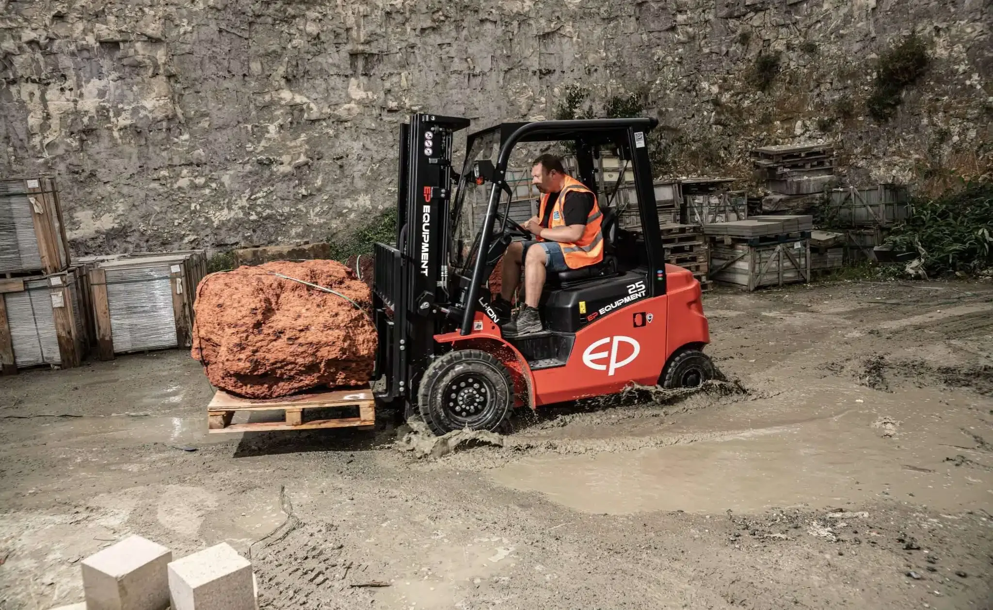 Un uomo sulla guida di un carrello elevatore con batteria al litio rosso trasporta un grande masso di pietra su un pallet in un'area di cantiere