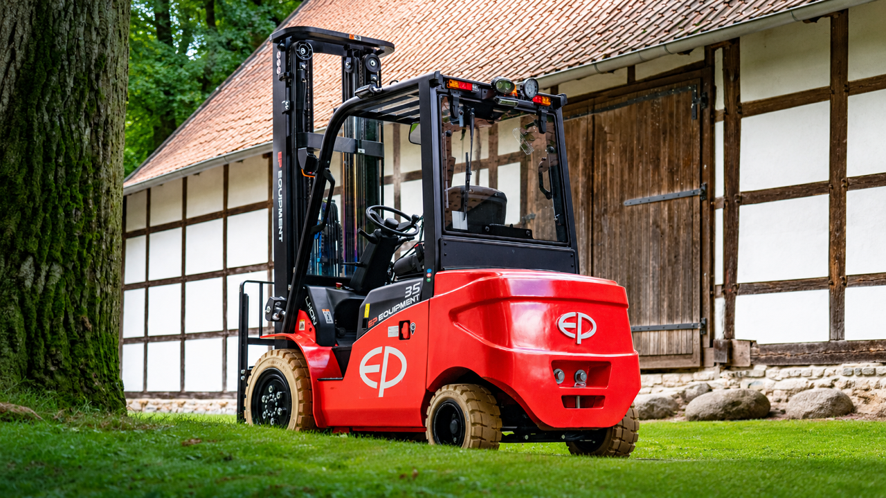 Un carrello elevatore con batterie al litio, rosso in un cortile con abitazioni in legno, accanto a un albero grande in un ambiente verde e all'aperto.