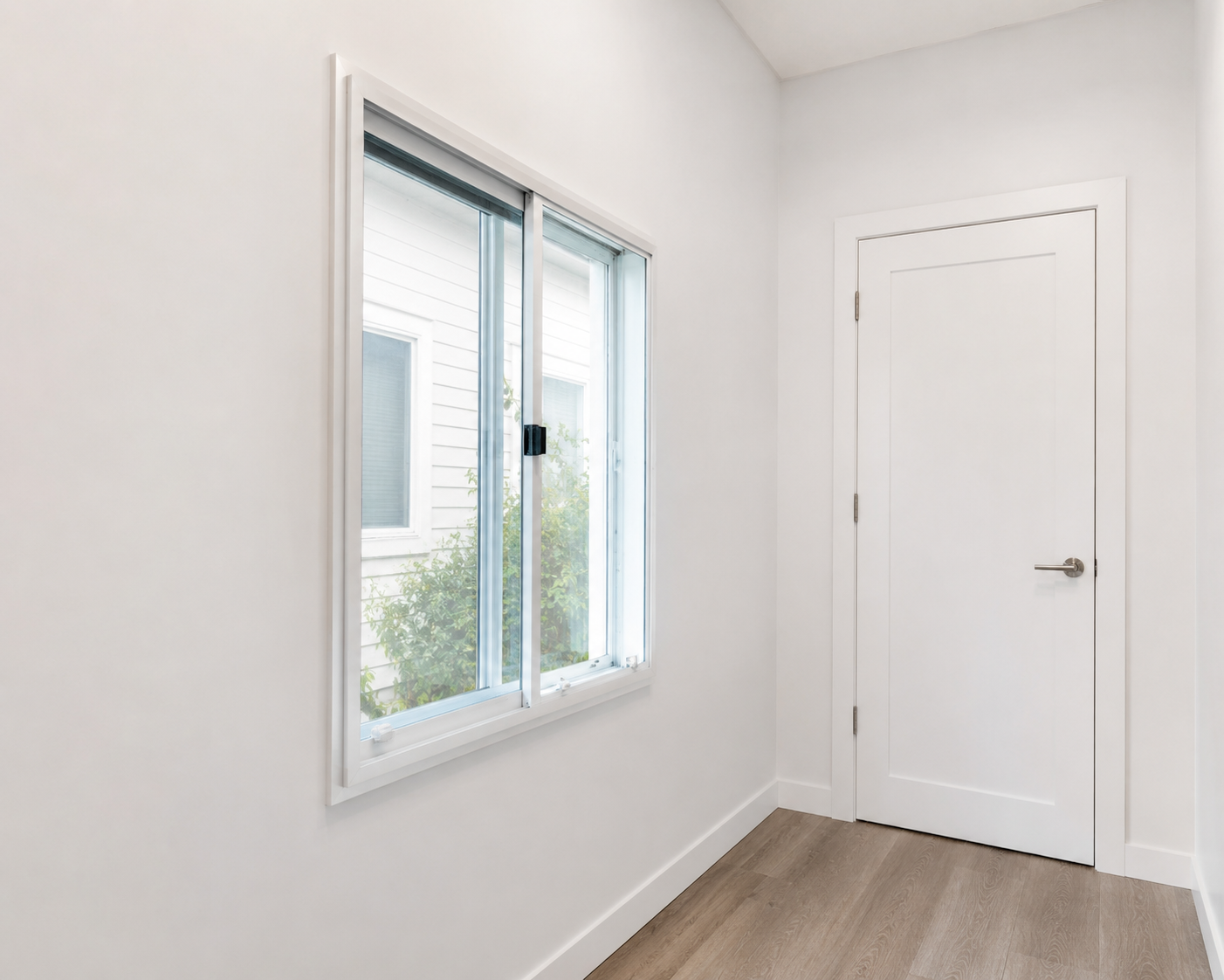 An interior view of a white room with a sliding glass window and a closed white door.
