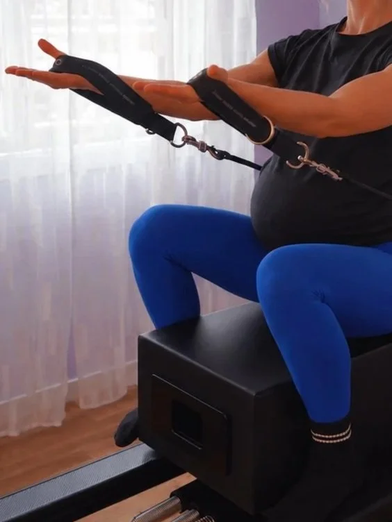 Pregnant woman on Pilates Reformer sitting on a box holding straps