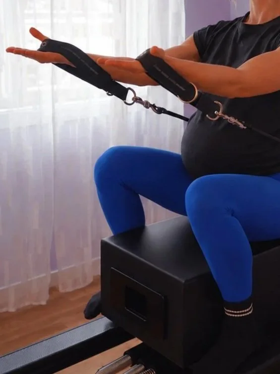 regnant woman on Pilates Reformer sitting on a box holding straps