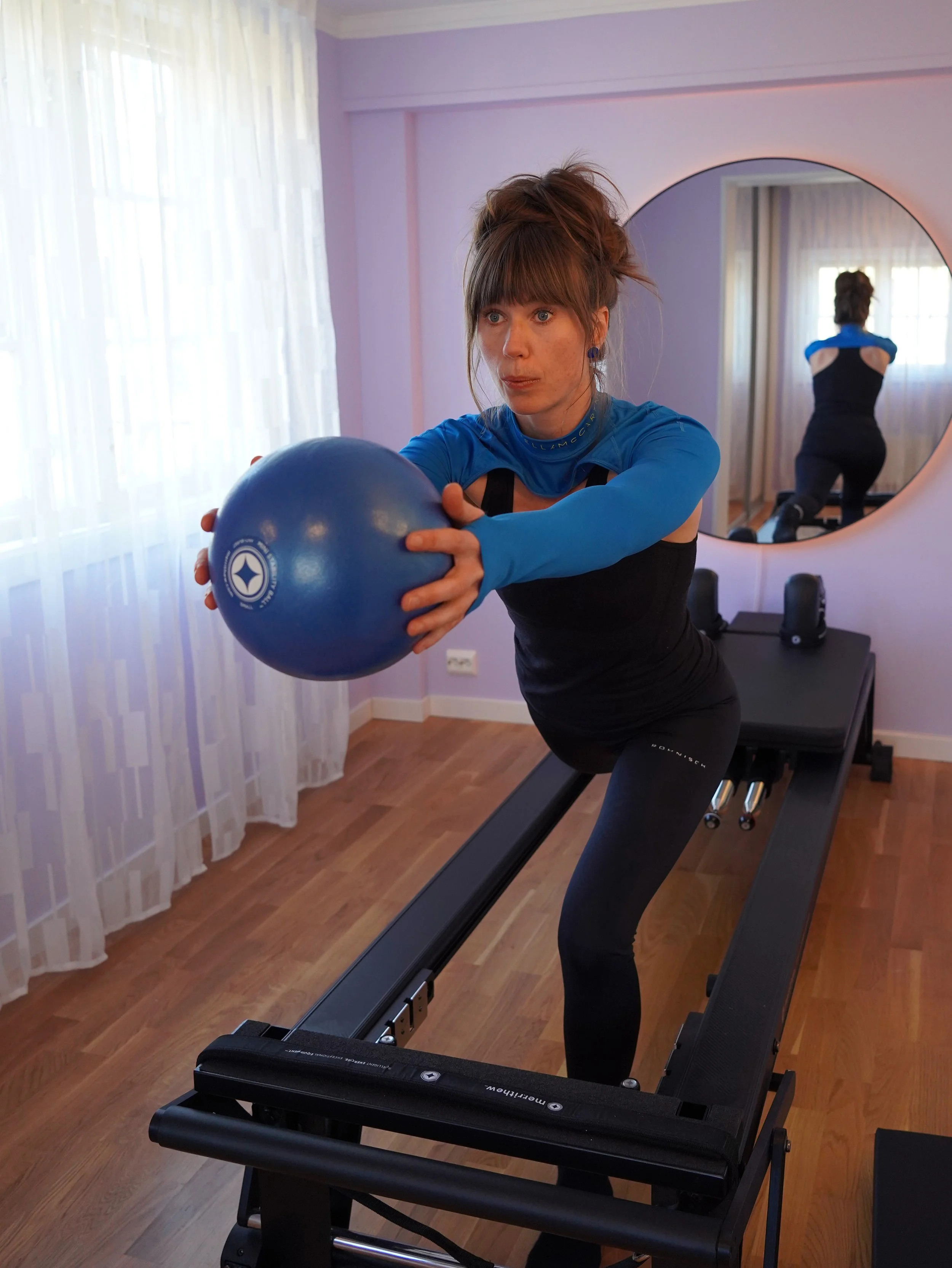 Woman on a Pilates Reformer holding a stability ball