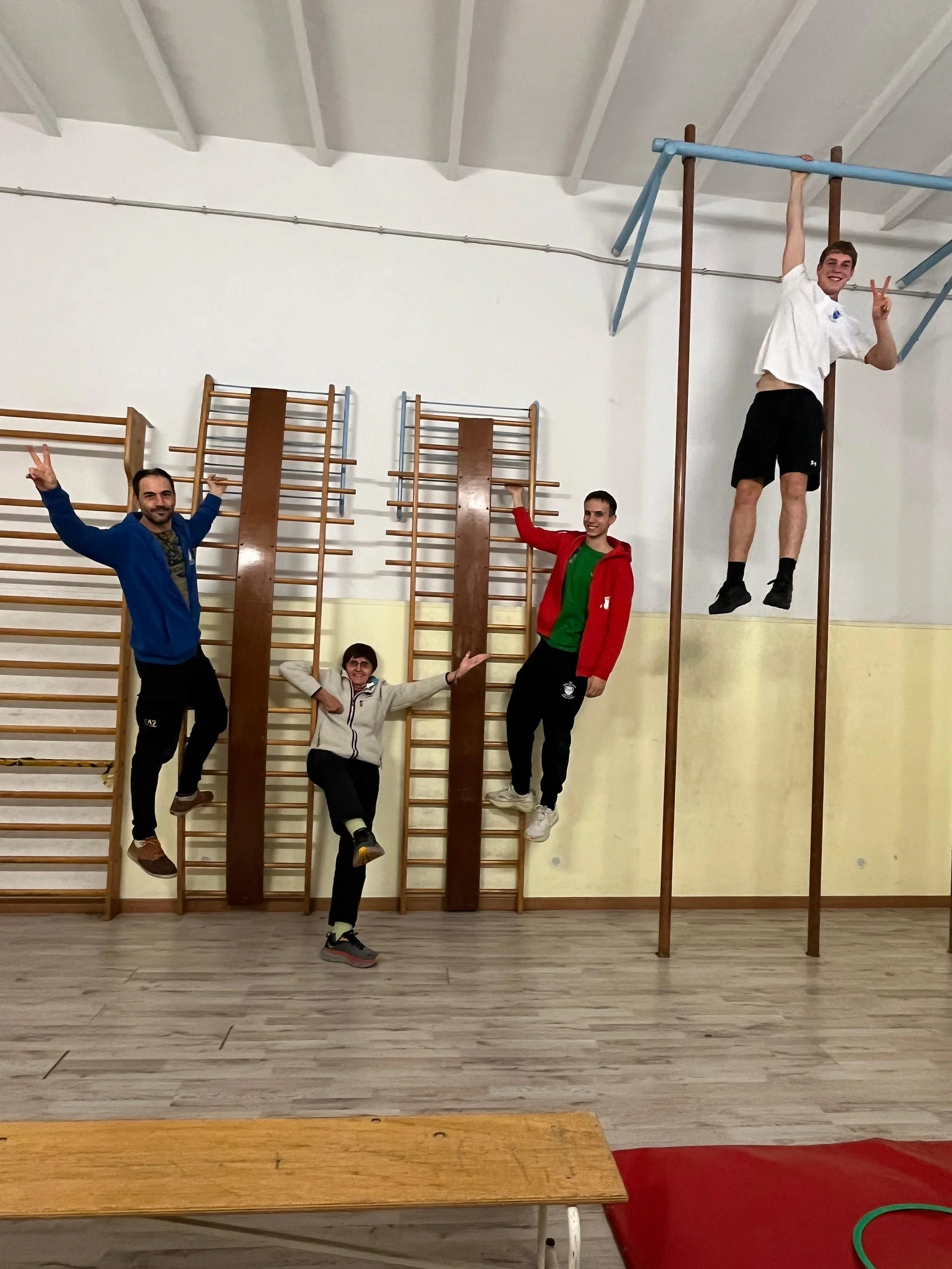 Cinque giovani in palestra, alcuni si tengono ai bastoni per l'esercizio e altri fanno pose divertenti, uno sorride e fa il gesto della vittoria con la mano