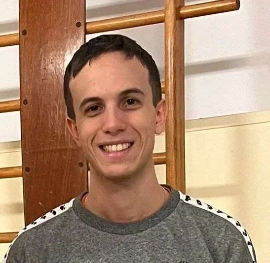 Ragazzo sorridente in palestra, con parete di aste di arrampicata in legno dietro