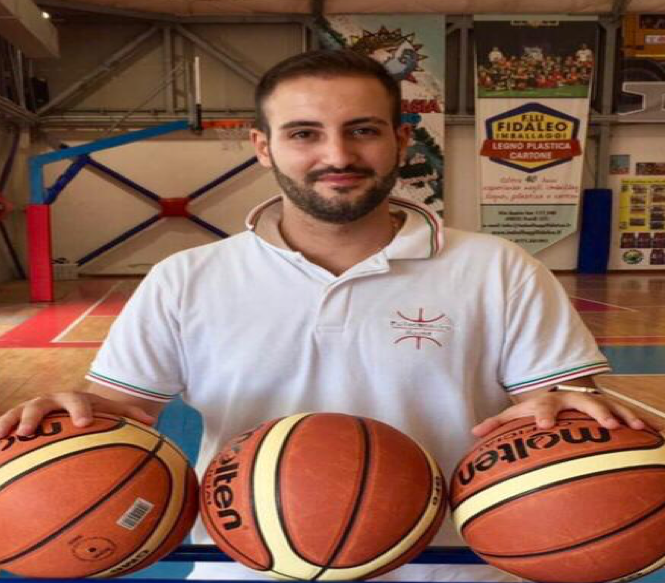 Uomo in abbigliamento sportivo con tre palloni da basket su un tavolo in palestra.