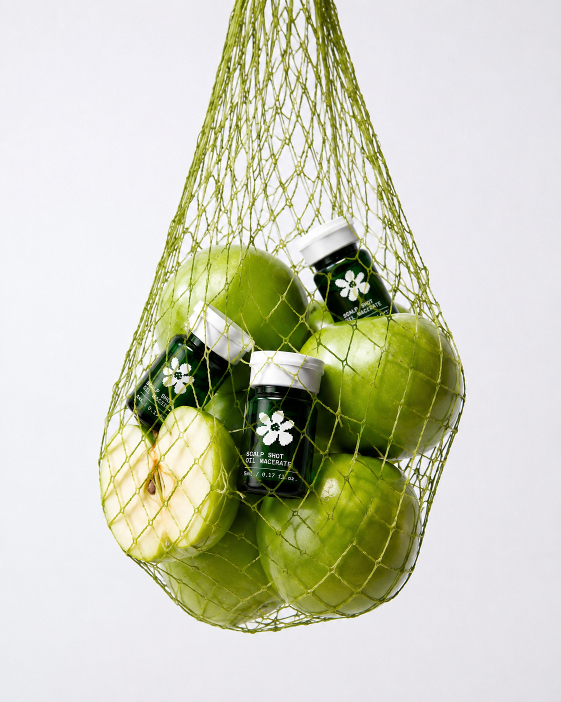 Pommes vertes et flacons de macérat d'huile OiliCraft, ingrédients botaniques utilisés dans le protocole capillaire.