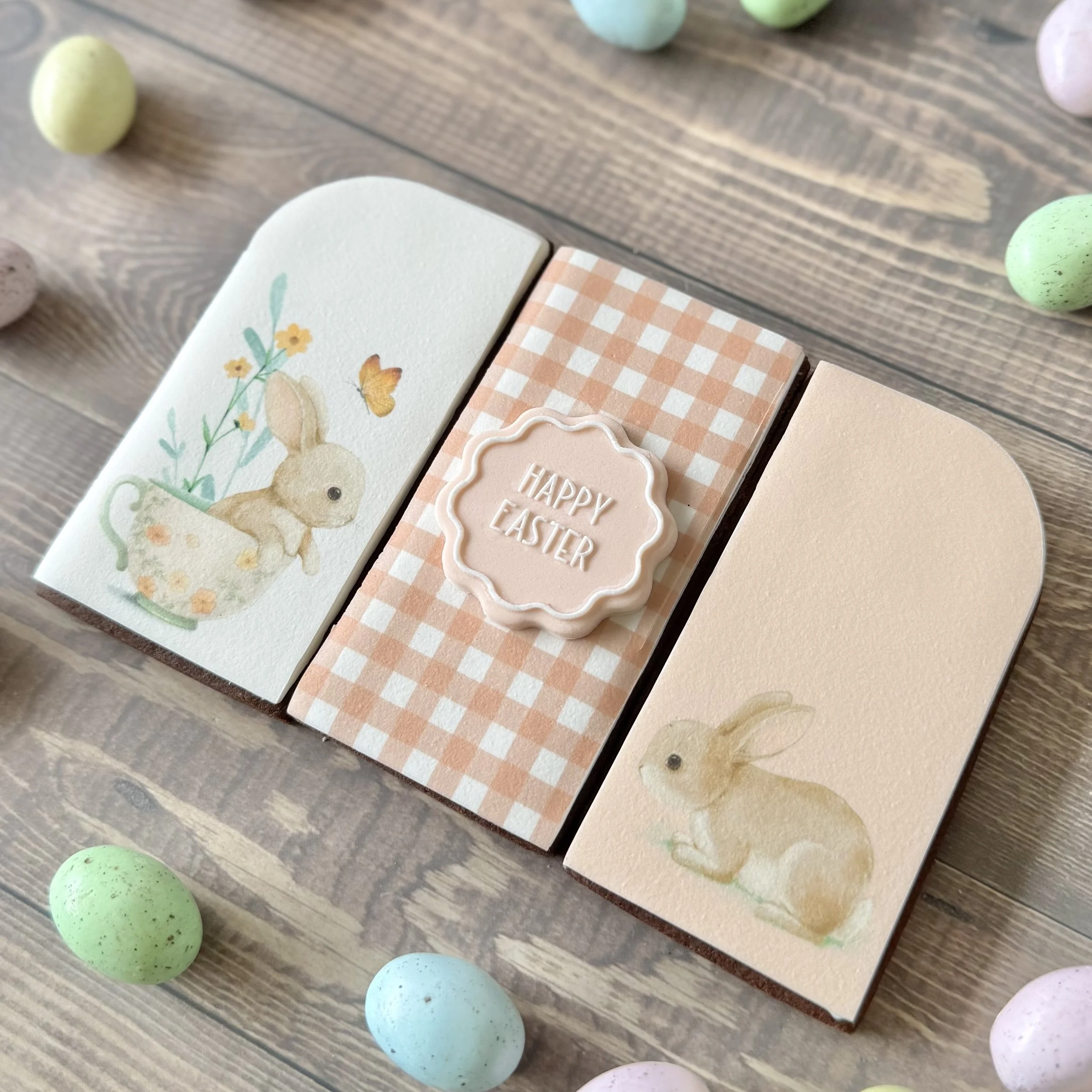 Colourful Easter eggs in pastel shades scattered on wooden surface with edible image cookies of cute bunnies