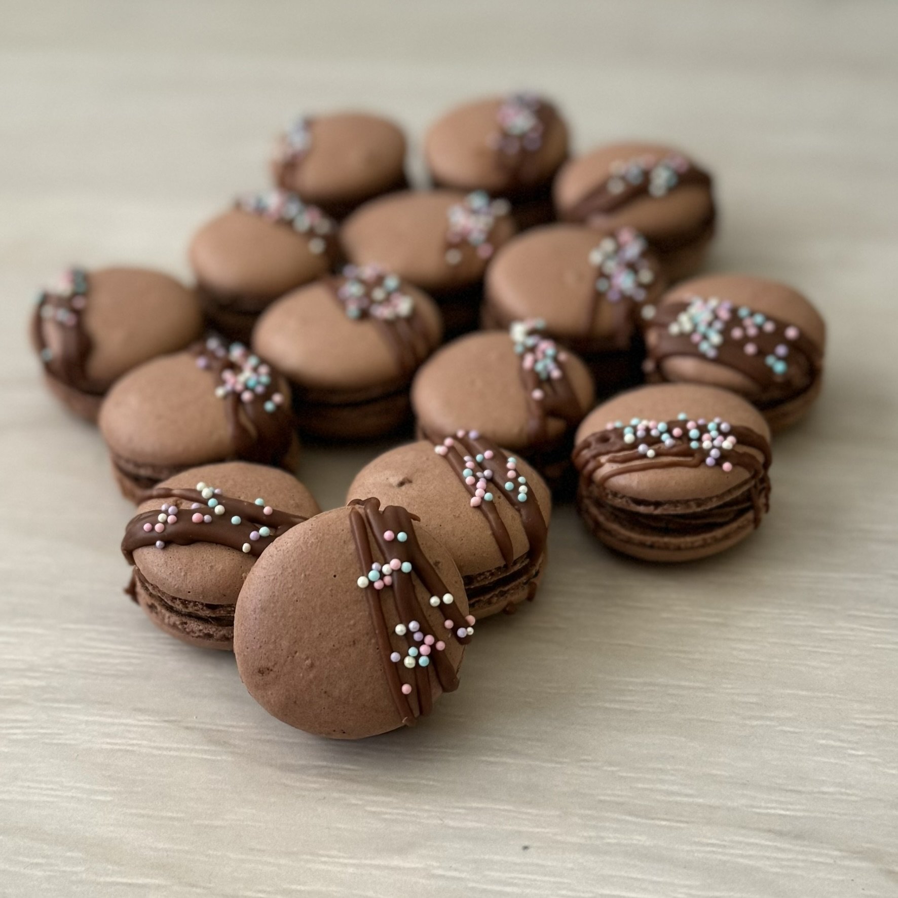 Chocolate macarons with a chocolate drizzle, sprinkled with colourful hundreds and thousands