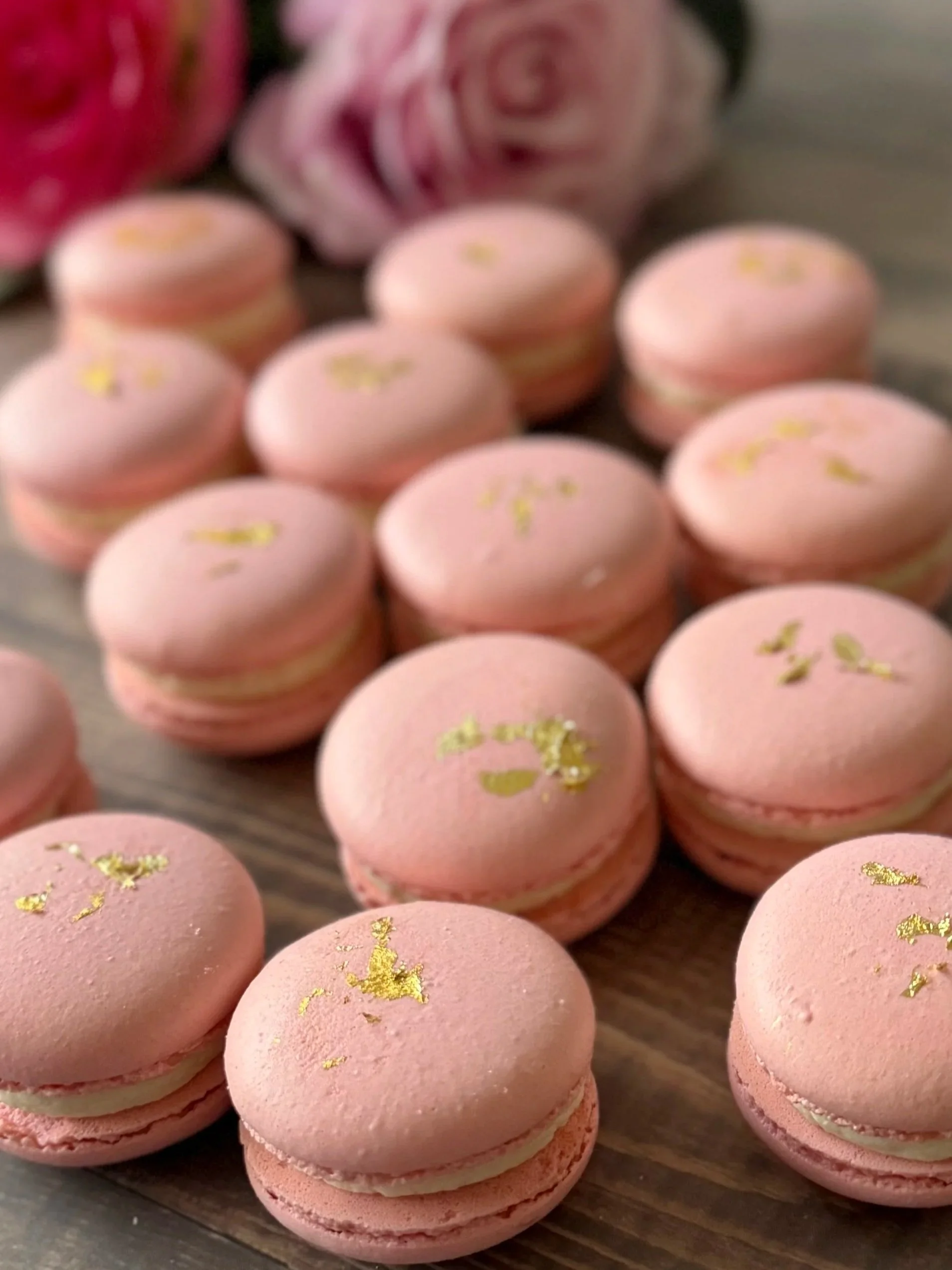 A close-up of pink macarons decorated with gold leaf on a wooden surface