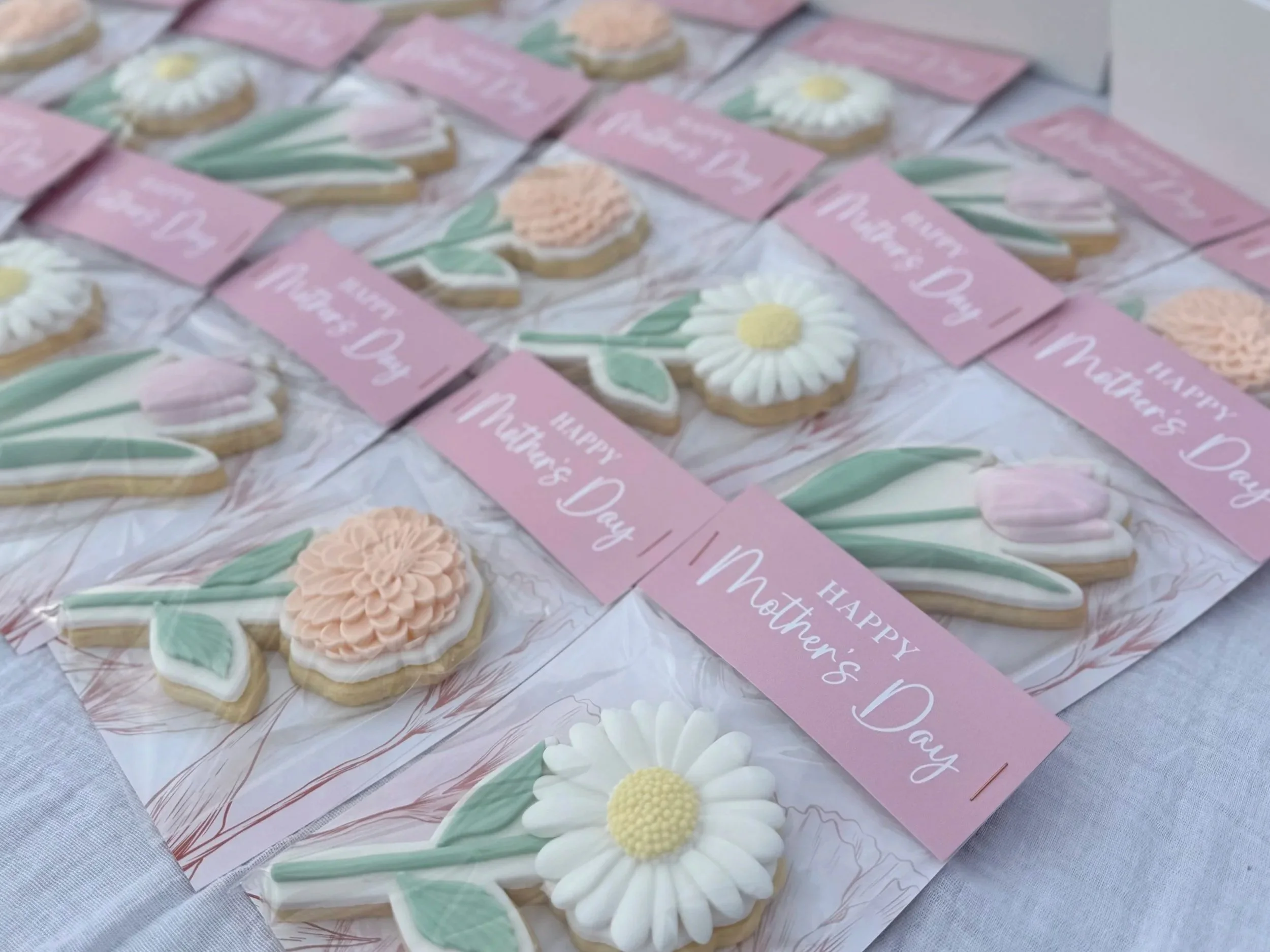 Cookie decorations with flowers and pink tags reading "Happy Mother's Day" arranged on a table for Mother's Day celebration