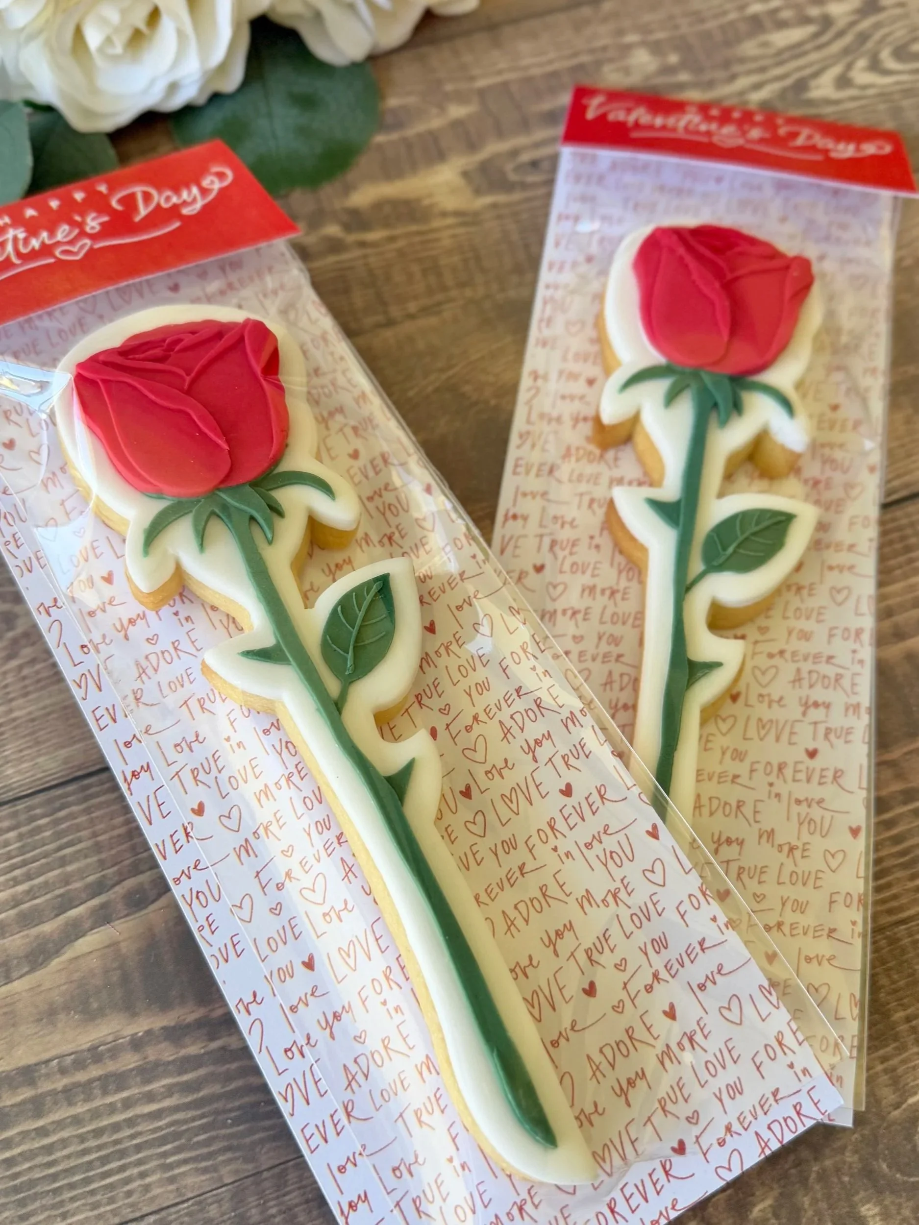 Long Stem Red Roses with red petals and green leaves, placed on Valentine's Day-themed wrappers with red and pink writing