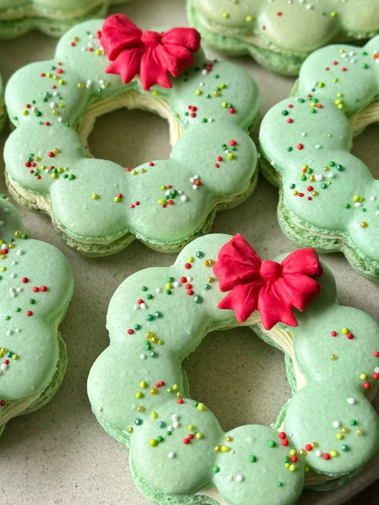 Green Christmas wreath macarons decorated with colourful sprinkles and a red bow