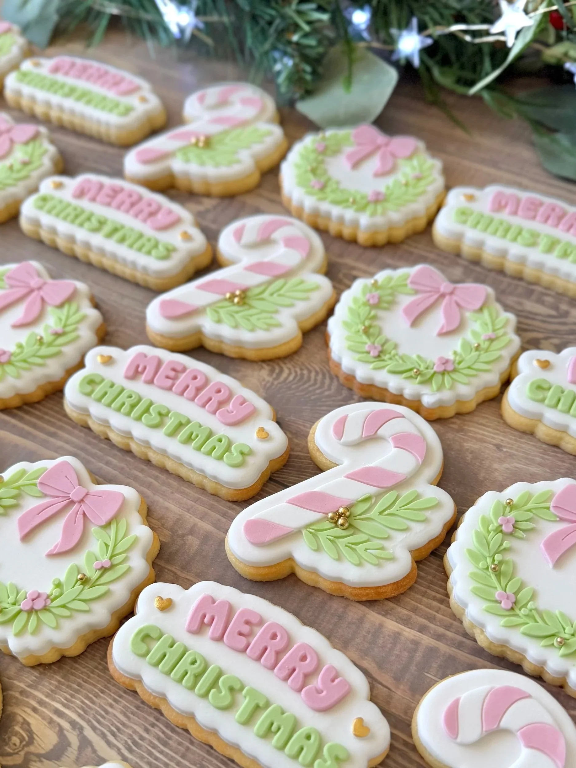 Decorative Christmas cookies with pastel pink, green, and white fondant, shaped like candy canes, bows, and festive sayings