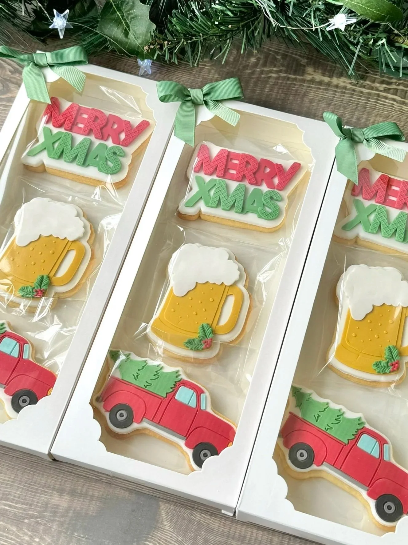 Vanilla sugar cookies decorated with Christmas themes, including cookies with the words "MERRY XMAS" in red and green fondant, cookies shaped like beer mugs with white foam and gold colour for the beer, and cookies shaped like red trucks carrying gre