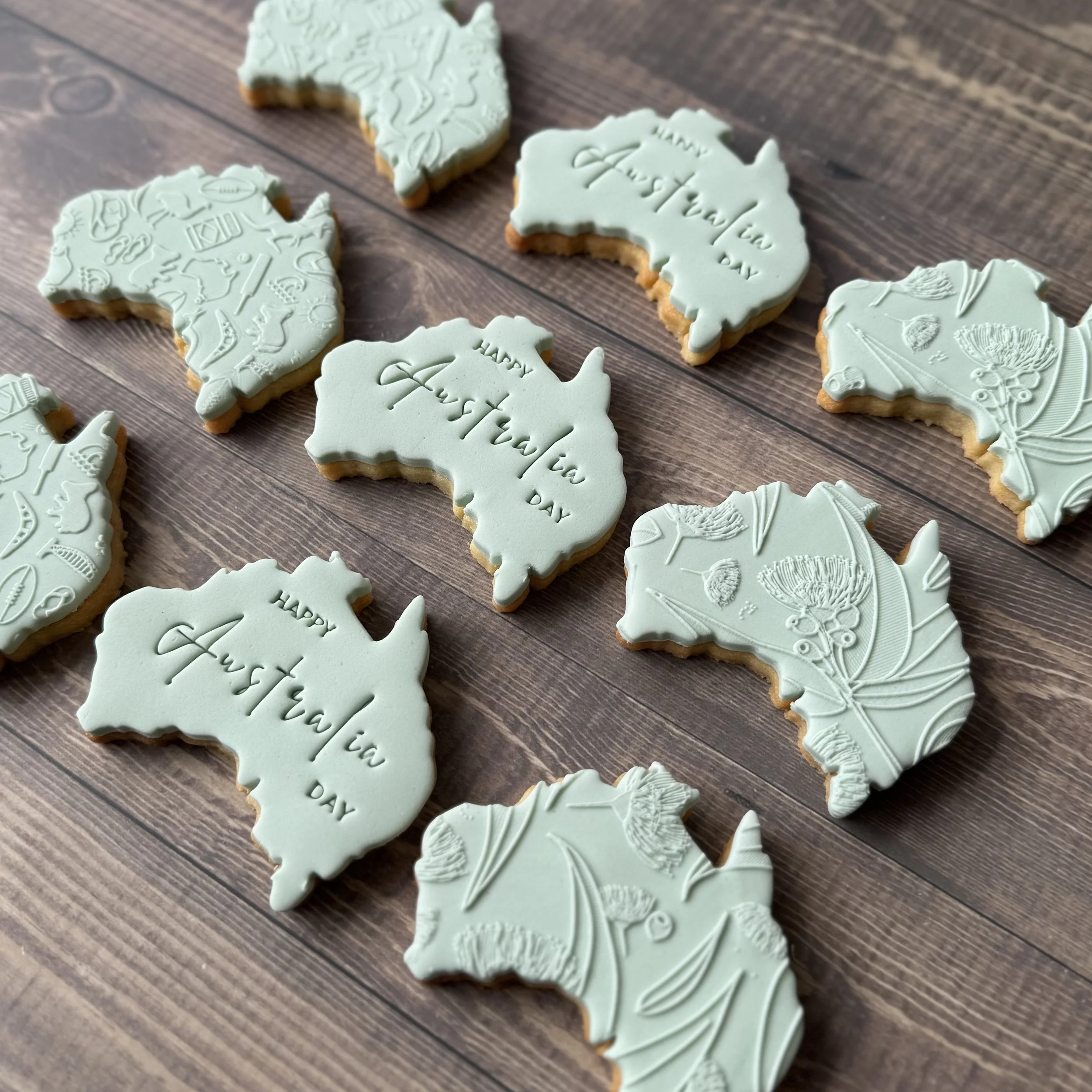 Sugar cookies in the shape of Australia. Some cookies have the words "HAPPY AUSTRALIA DAY" and others feature embossed designs of Australian-related symbols - wattle and gumtrees