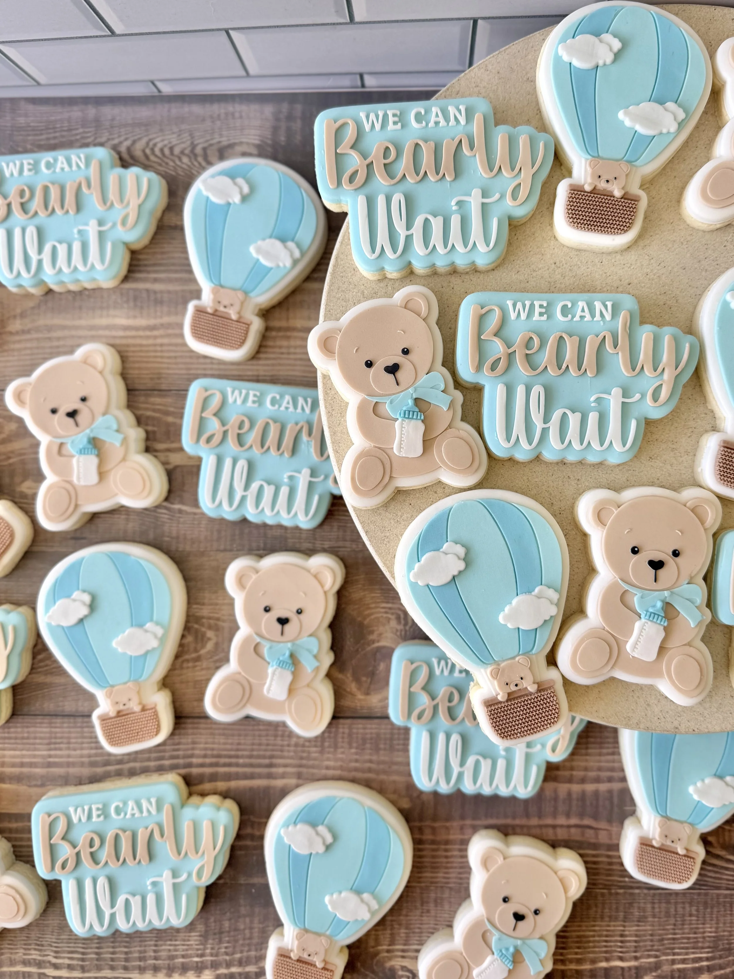 Decorative baby shower cookies with pastel blue, white, and beige colours featuring teddy bears, hot air balloons, and the phrase "We can bearly wait"