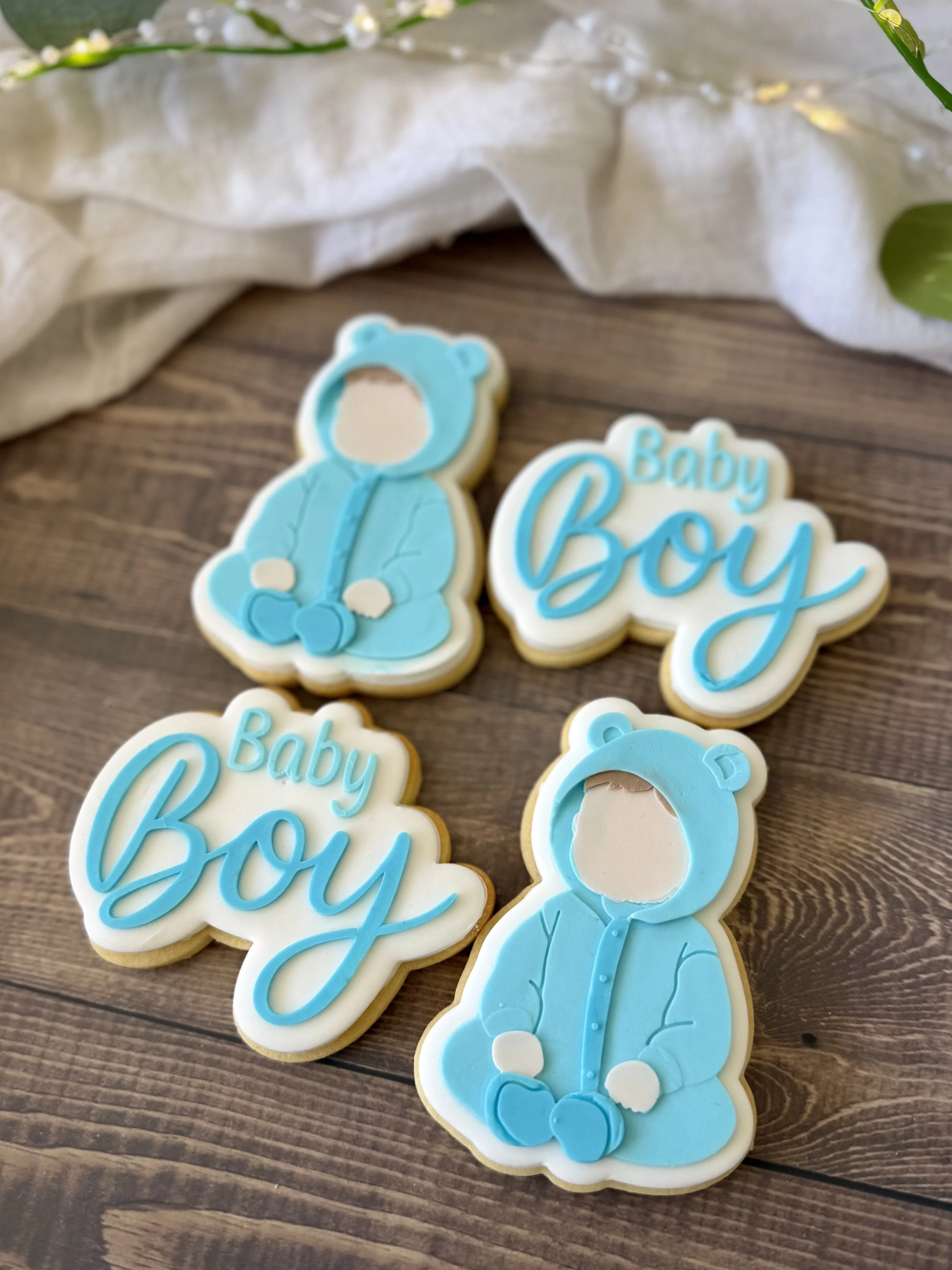 Handcrafted baby boy sugar cookies featuring a sweet baby in a blue bear onesie and matching Baby Boy lettering, decorated with layered fondant in soft blue and white.