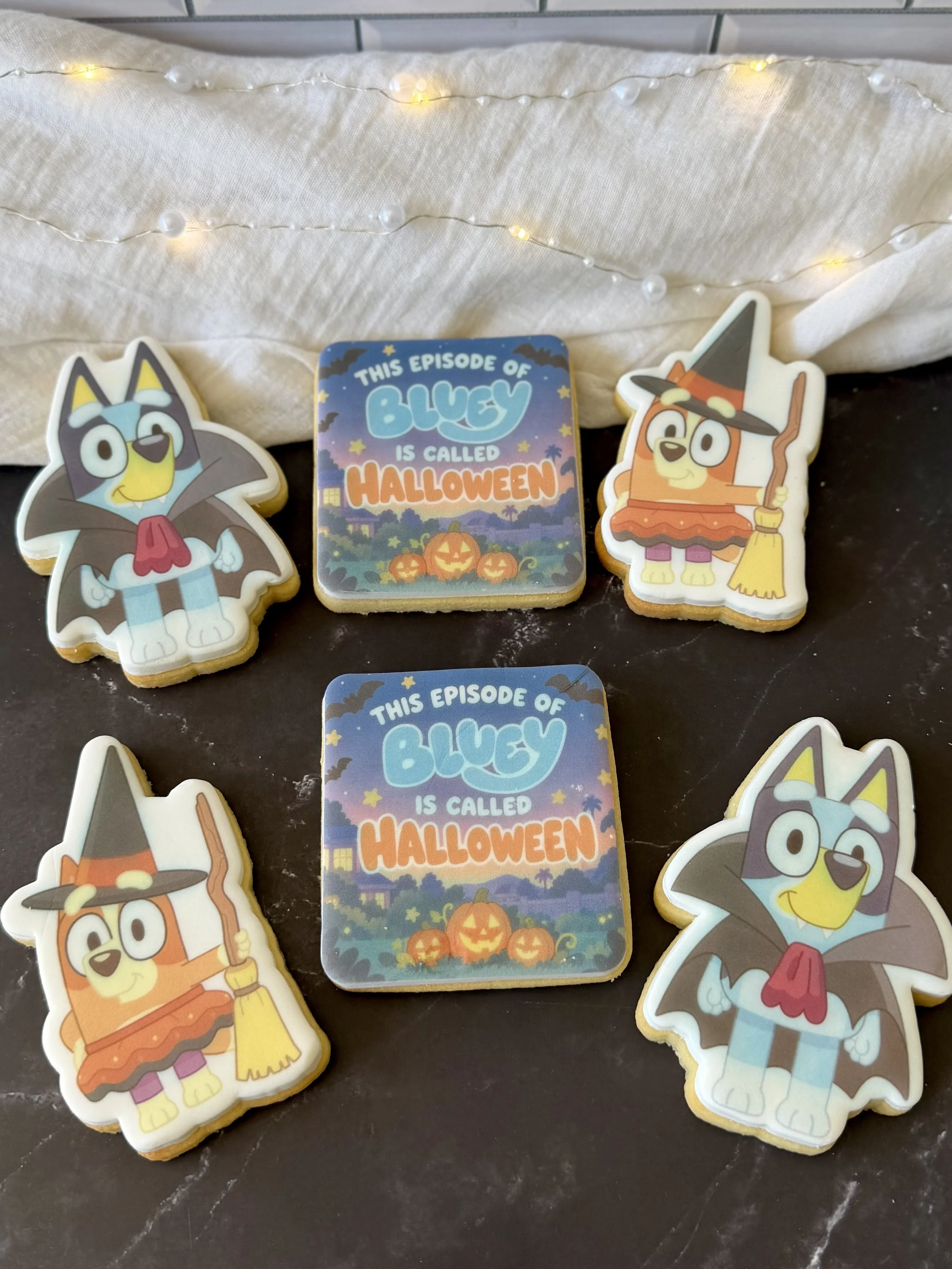 Bluey and Bingo Halloween-themed sugar cookies featuring vampire and witch costumes, alongside an episode title cookie