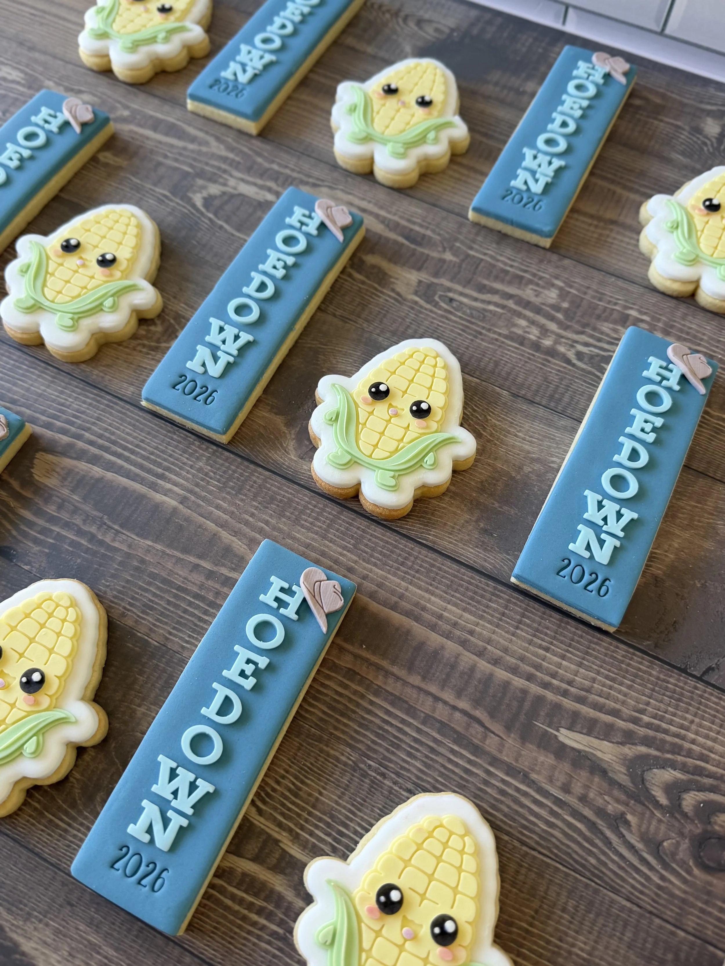 Decorative cookies shaped like a cute smiling corn cob and rectangular cookies with the word "Hoedown" and the year "2026" written on them