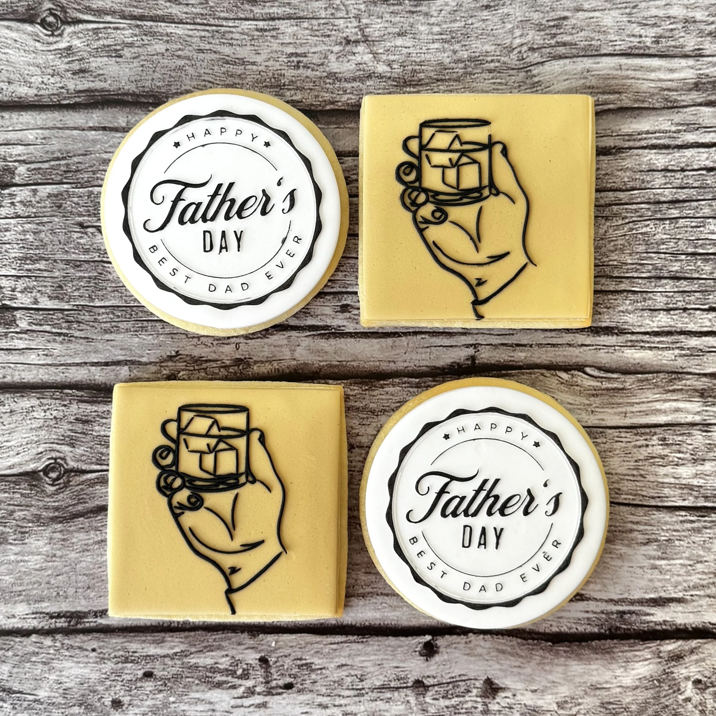 Decorative cookies for Father's Day, with one round cookie saying 'Happy Father's Day' and another rectangular cookie with a black outline of a hand holding a mug on yellow background, all placed on a rustic wooden surface