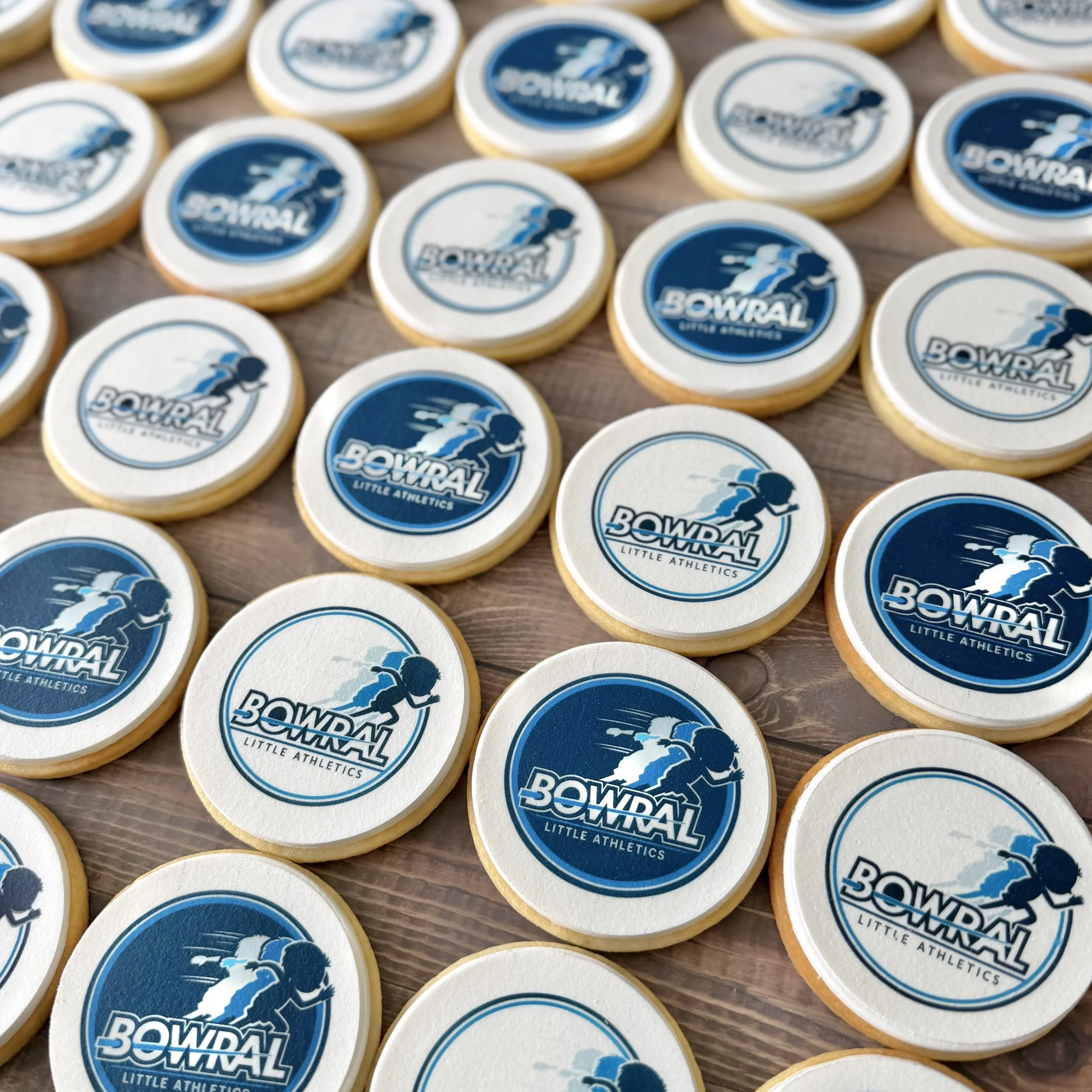 Close-up view of multiple round cookies with blue and white logo that reads "Bowral Little Athletics" featuring a silhouette of a young athlete running