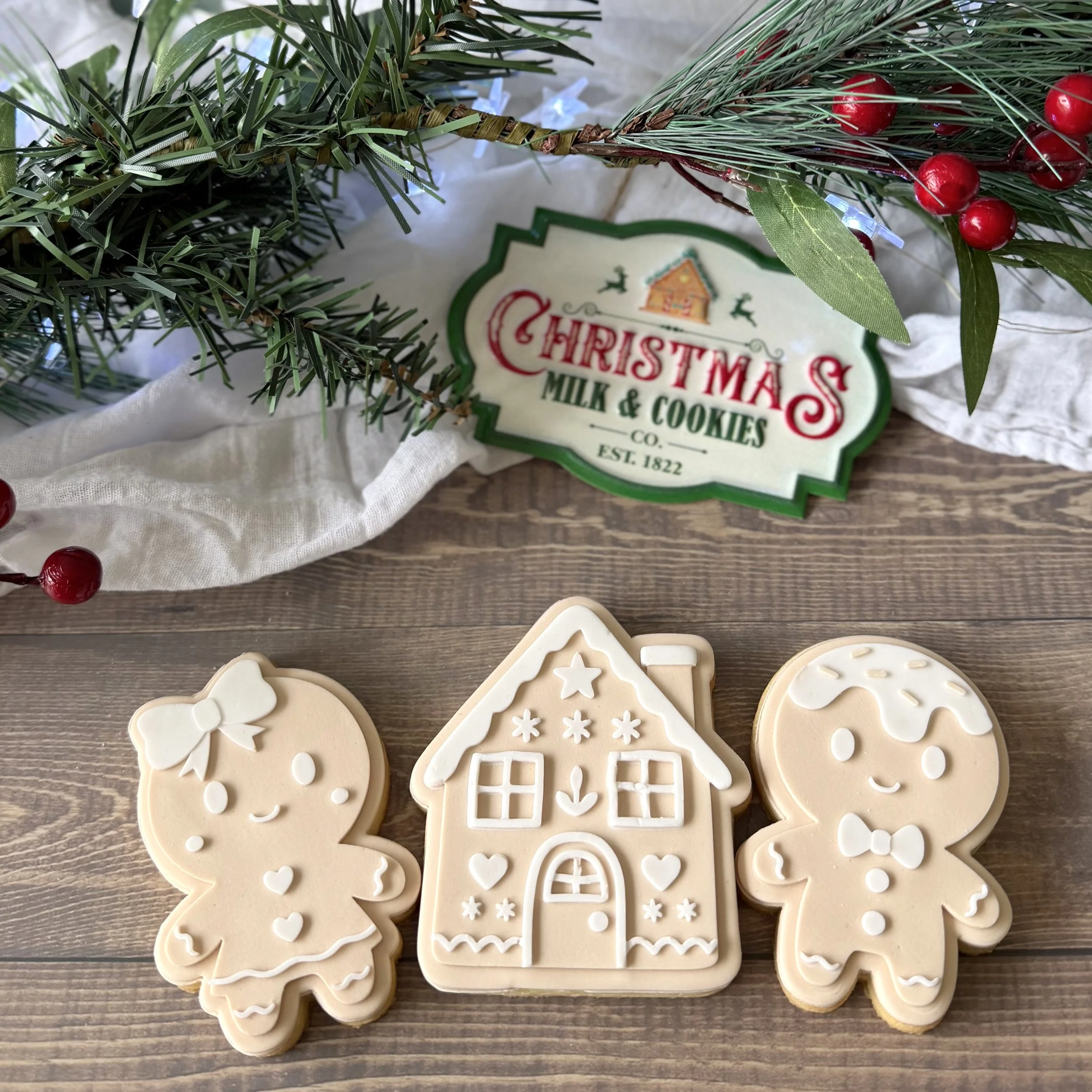 Decorative holiday gingerbread style cookies with Christmas-themed designs on a wooden surface. A Christmas wreath with red berries and green leaves is in the background.