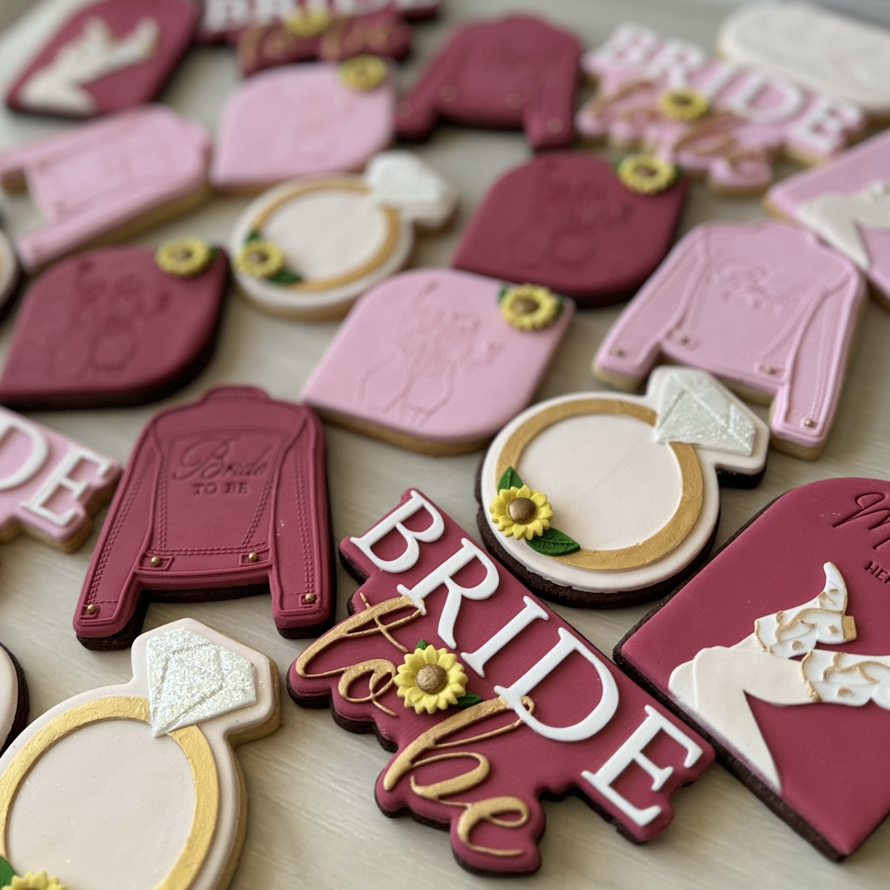 Custom pink, burgundy and gold Hen's party cookies featuring bride-to-be designs, engagement rings and sunflowers