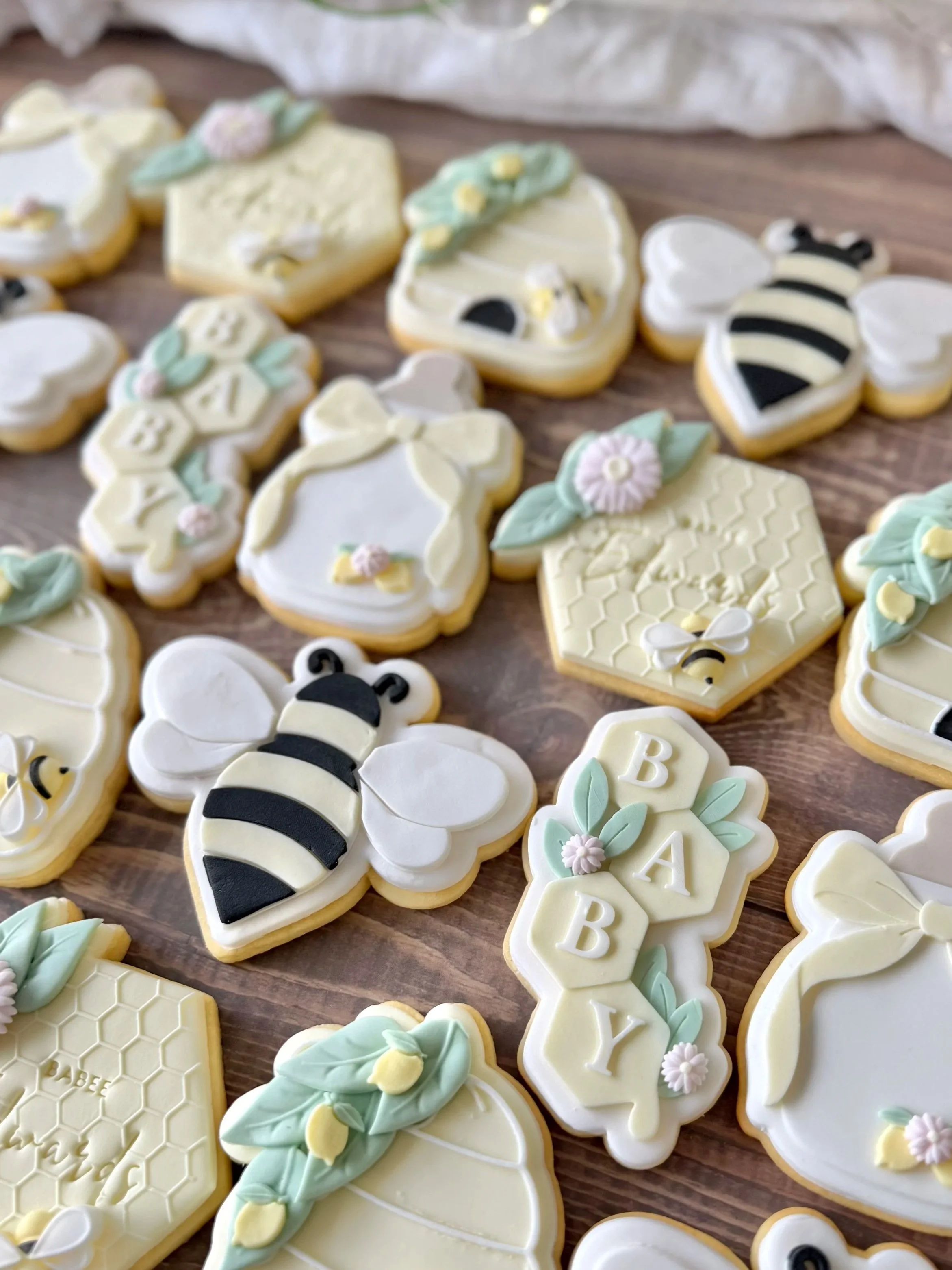 Decorative baby shower cookies with bee, honeycomb, and floral designs on a wooden surface