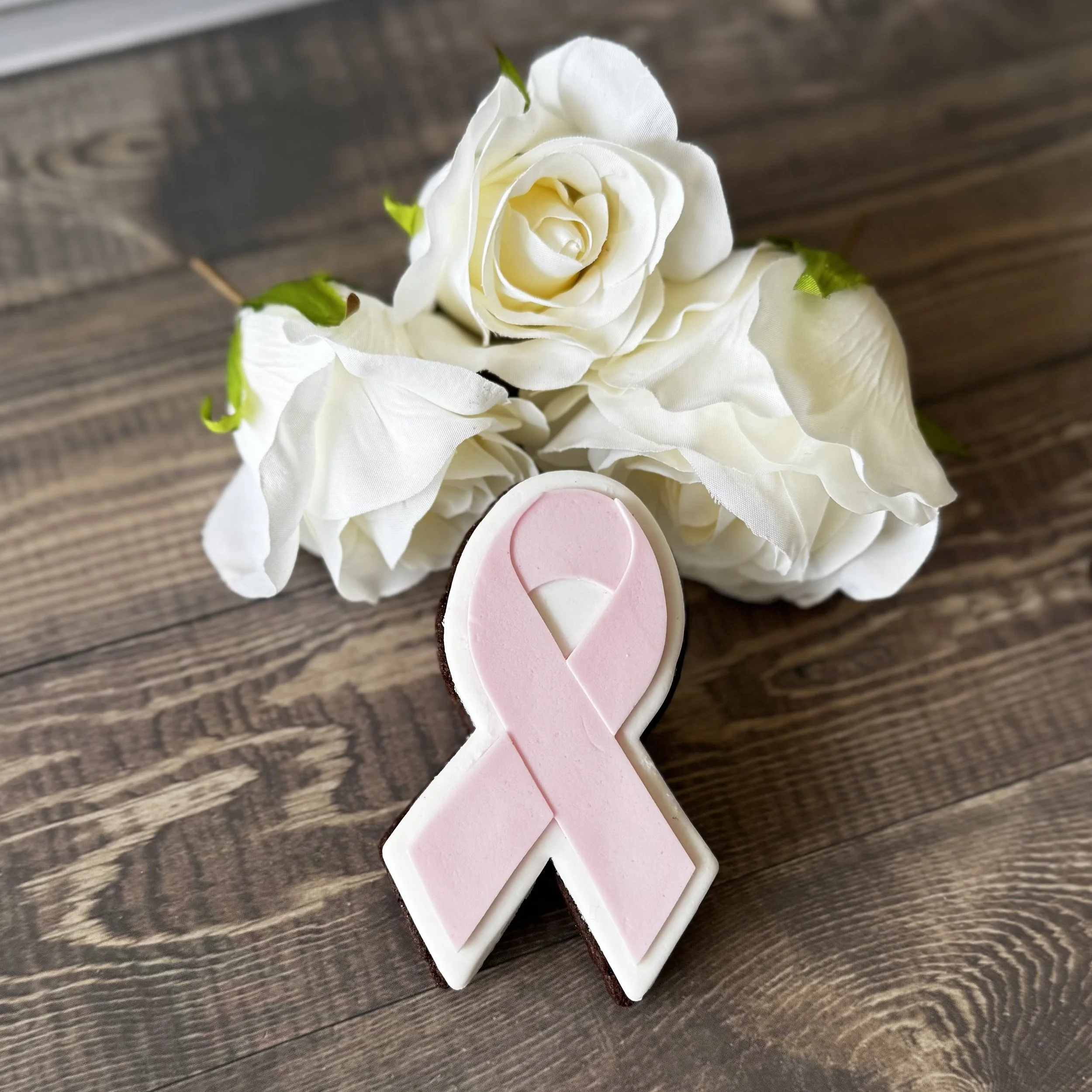 Artificial white roses with green leaves and a pink ribbon cookie for Breast Cancer Awareness