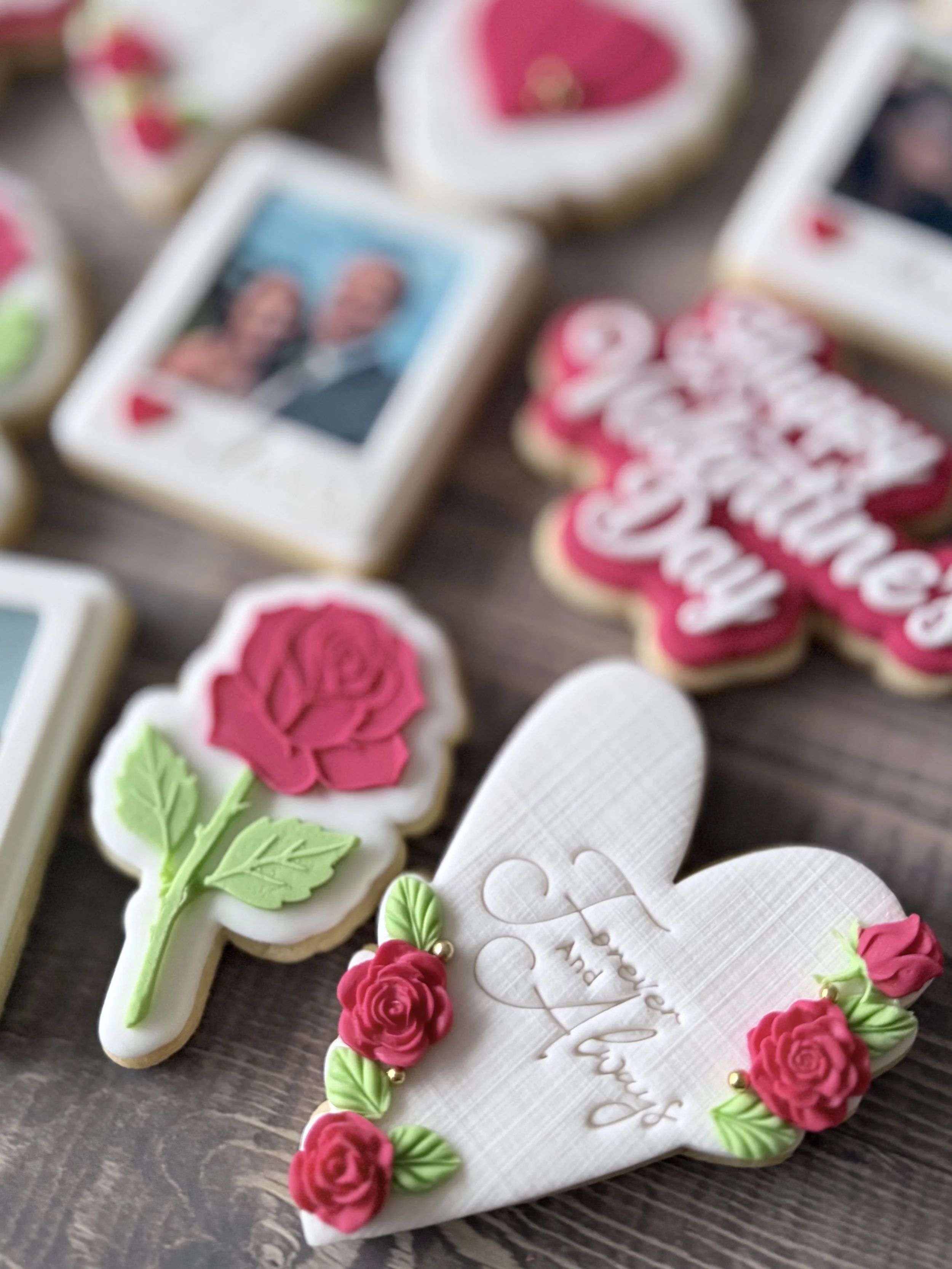 Decorative cookies with floral and love-themed designs, including roses, hearts, and a framed photo with two people for Valentine's Day