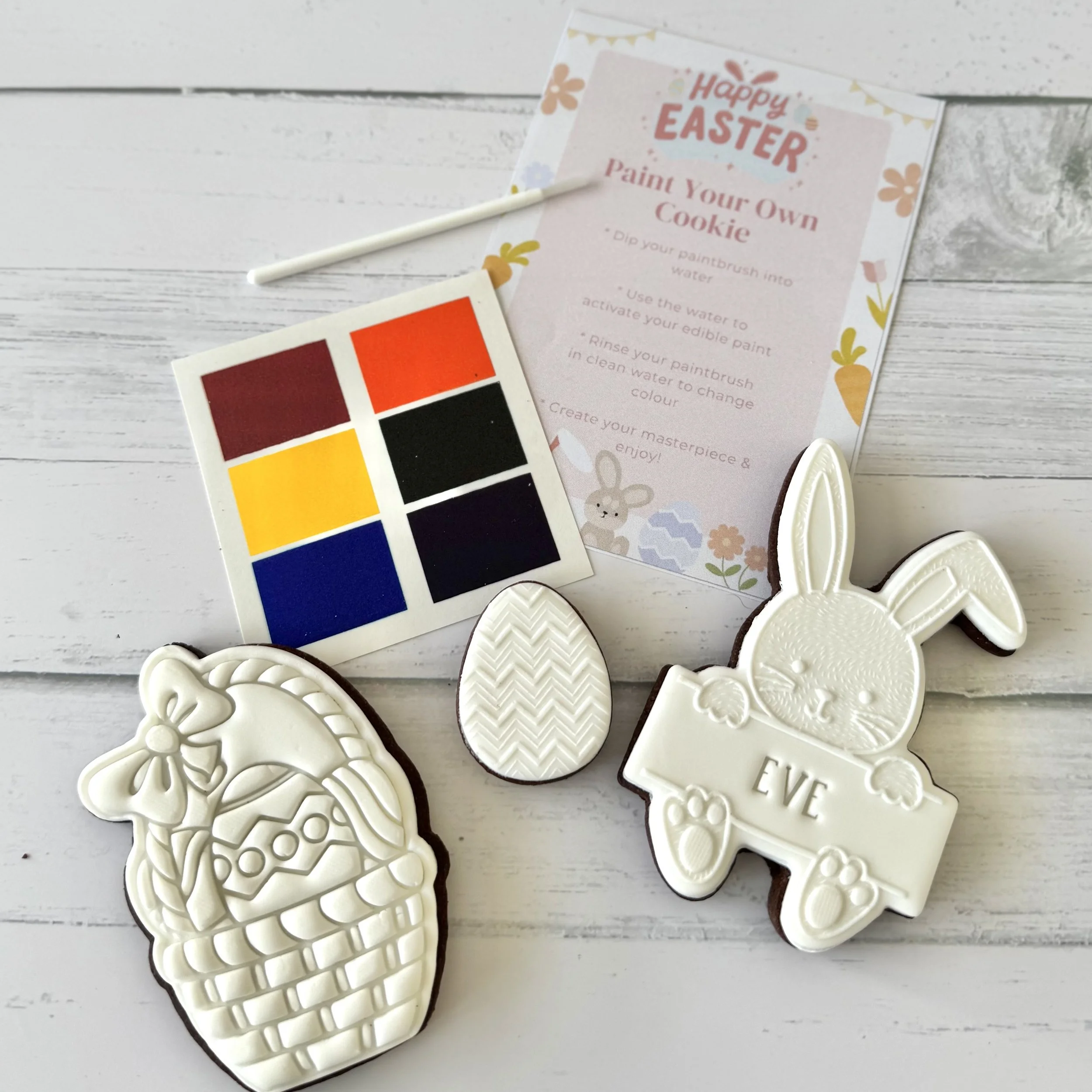 White chocolate bunny cookies decorated with intricate bunny and egg designs arranged on a white wooden surface, with Easter-themed colouring and decorating instructions on a paper next to them