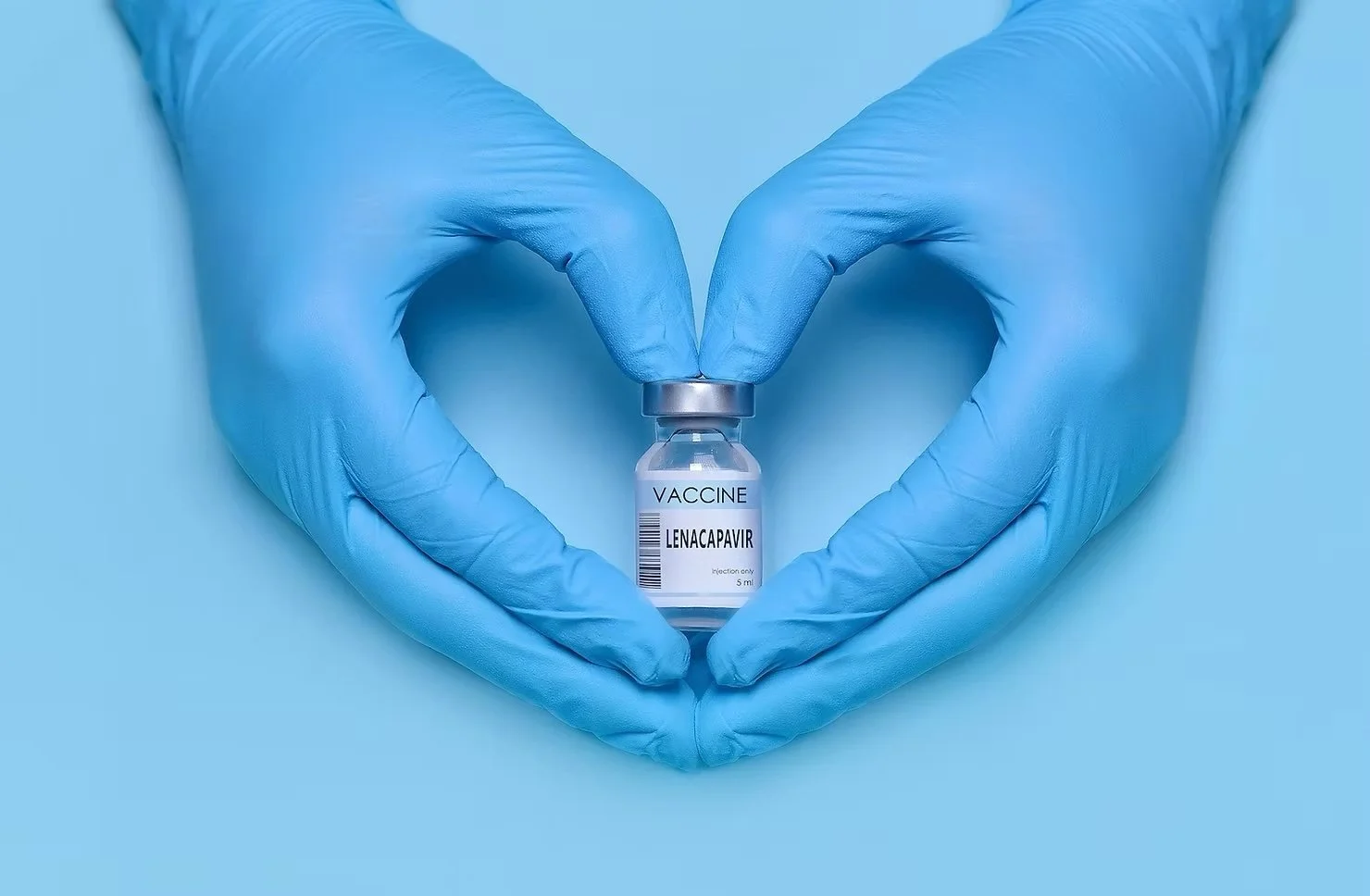 Two hands wearing blue medical gloves forming a heart shape around a small vial labeled 'Lenacapavir' with the word 'Vaccine' at the top, set against a light blue background.