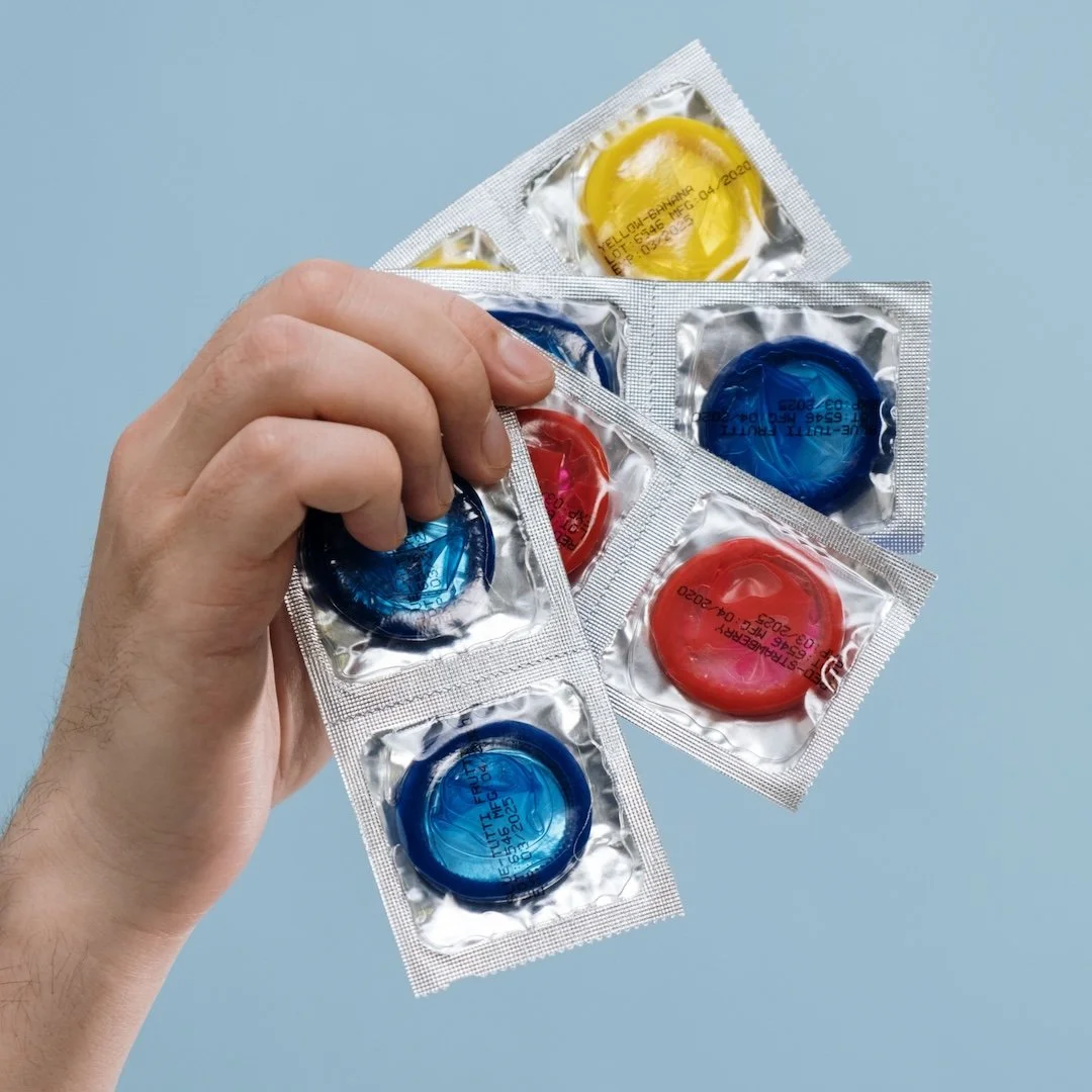 Hand holding a handful of colorful condom packets against a light blue background.