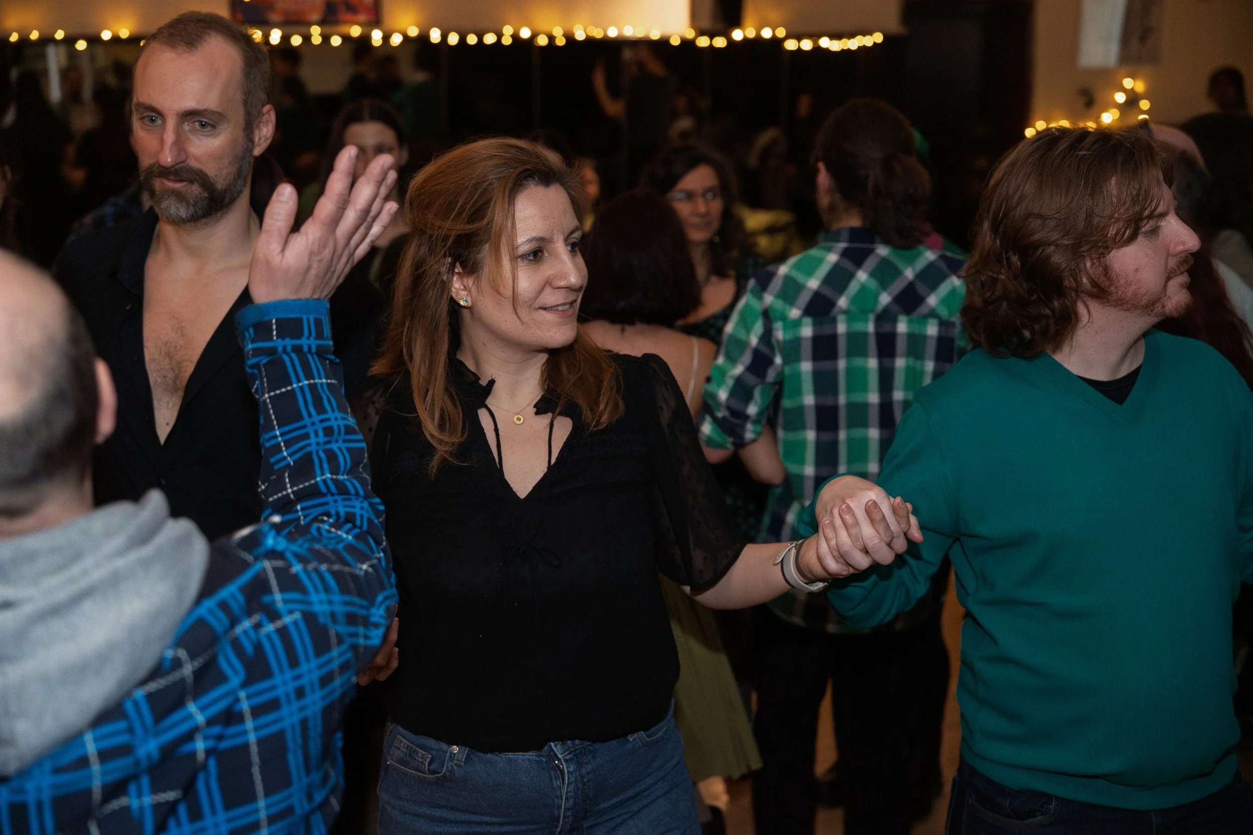 People holding hands while dancing at an indoor party with warm lighting and string lights in the background.
