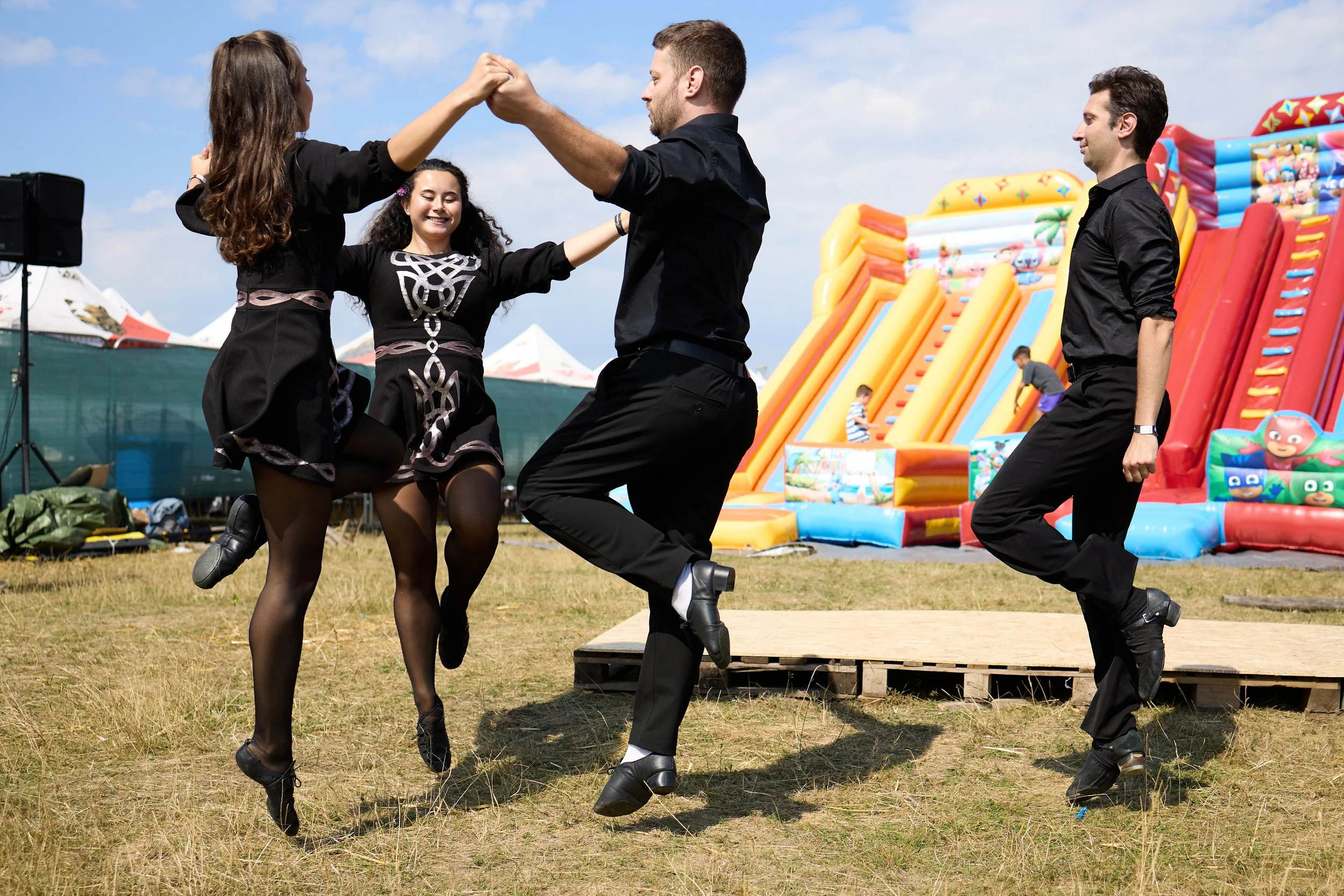 Four people dancing in a field at an outdoor event with inflatable slides in the background.