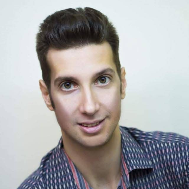 Portrait of a young man with dark hair, wearing a patterned shirt, smiling at the camera.