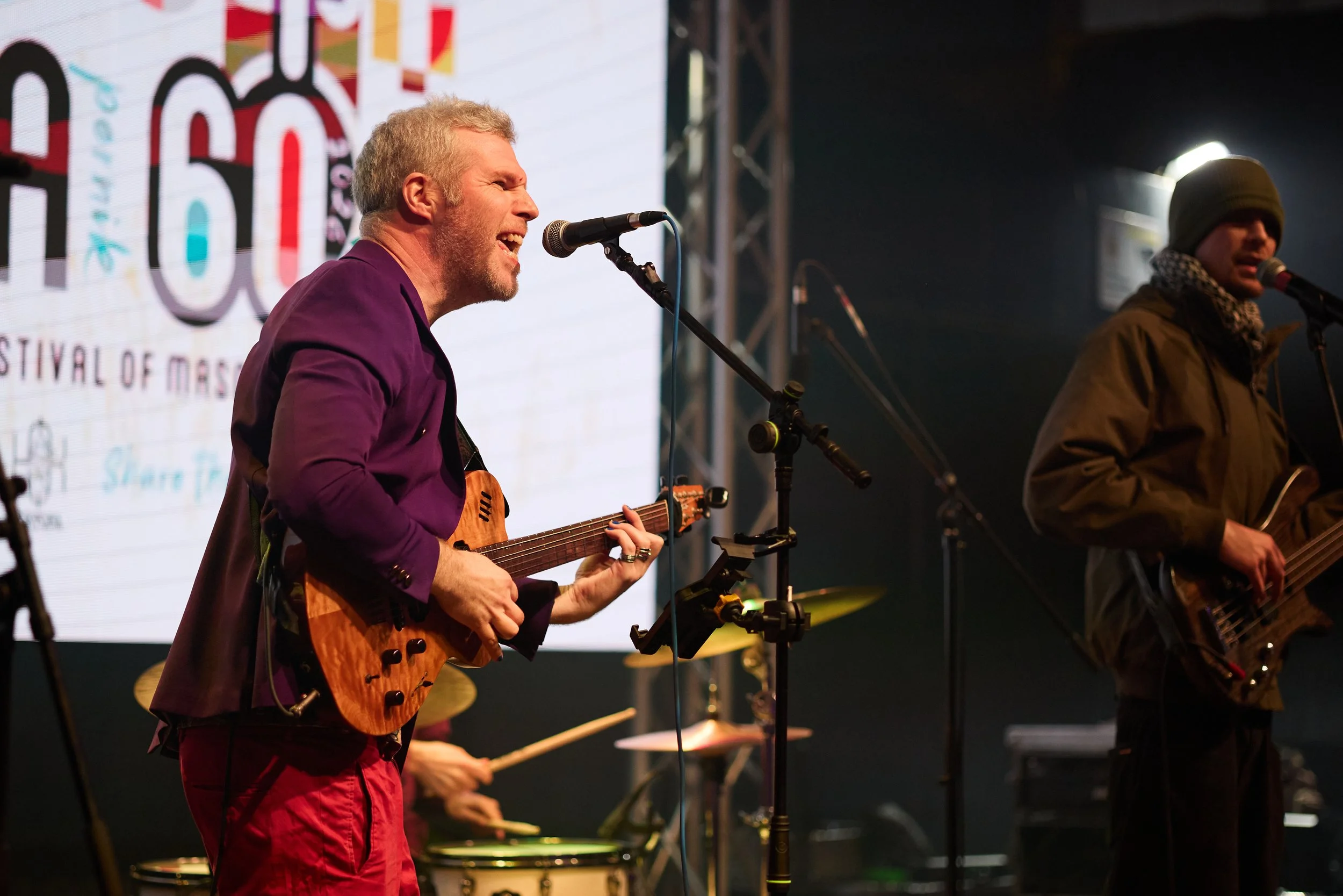 A man with a guitar singing into a microphone during a live performance.