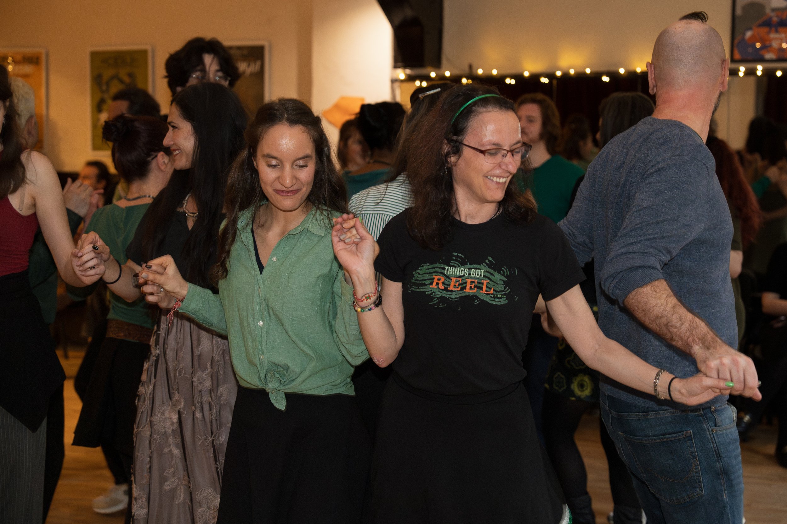 People holding hands and dancing at a social gathering or party in a room with string lights.