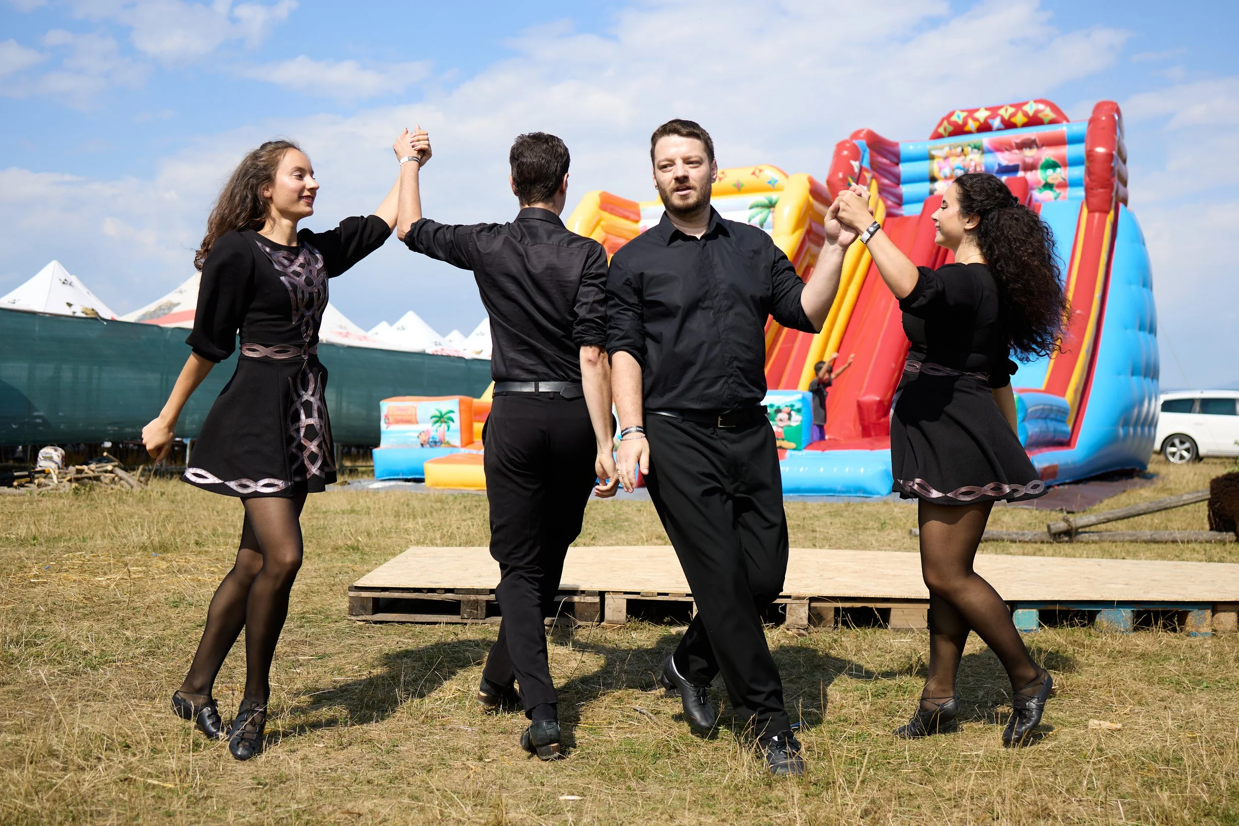 Four people dancing outdoors in front of a colorful inflatable slide at a fair or carnival.