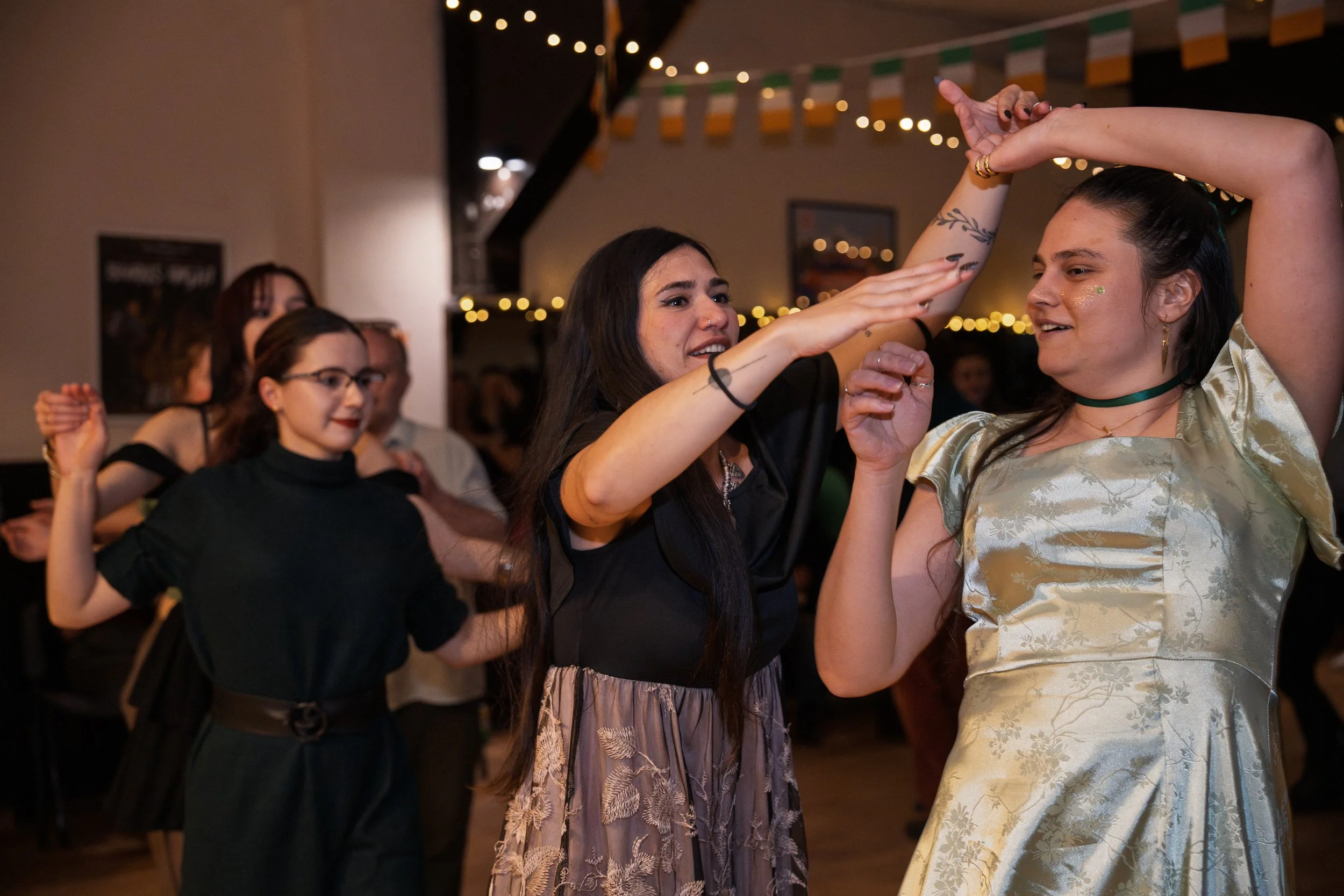 People dancing at a party with string lights and Irish flags hanging in the background.
