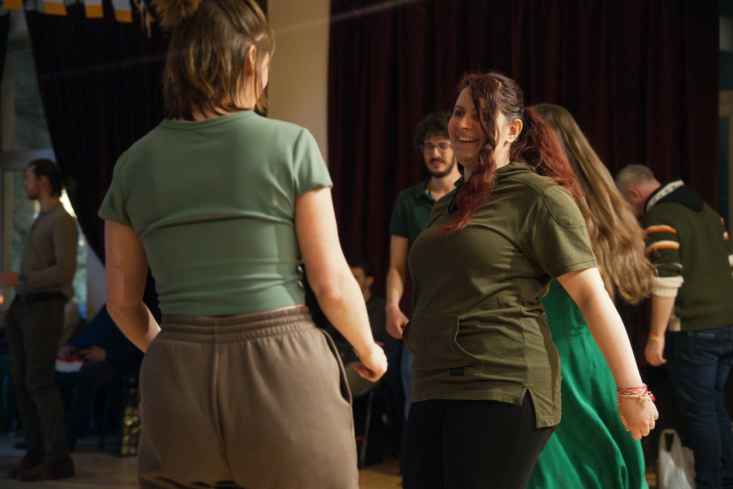 People dancing and socializing indoors, with a focus on two women in the foreground and others in the background.