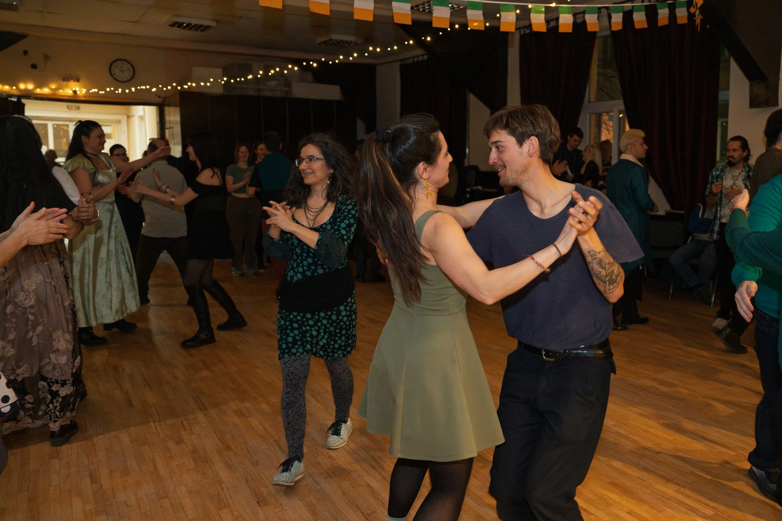 People dancing at a social event in a dimly lit room decorated with string lights and patriotic banners.