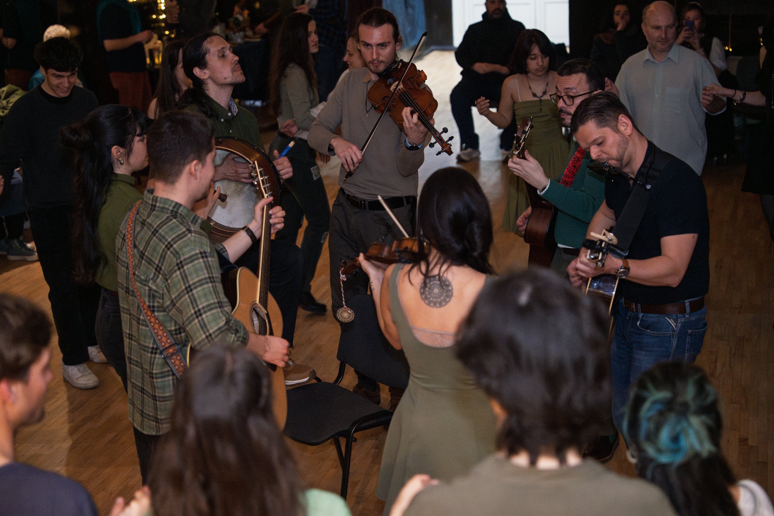 A group of musicians performing at an indoor event, with some people playing guitars and a violin, surrounded by an audience.