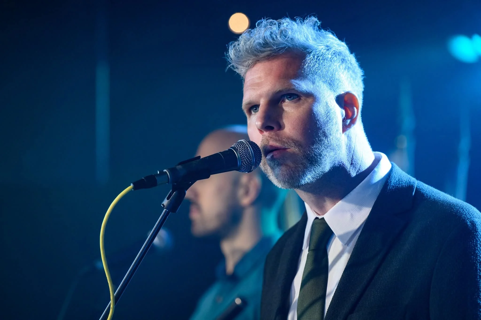 A man with gray hair and a beard singing into a microphone at a music event.
