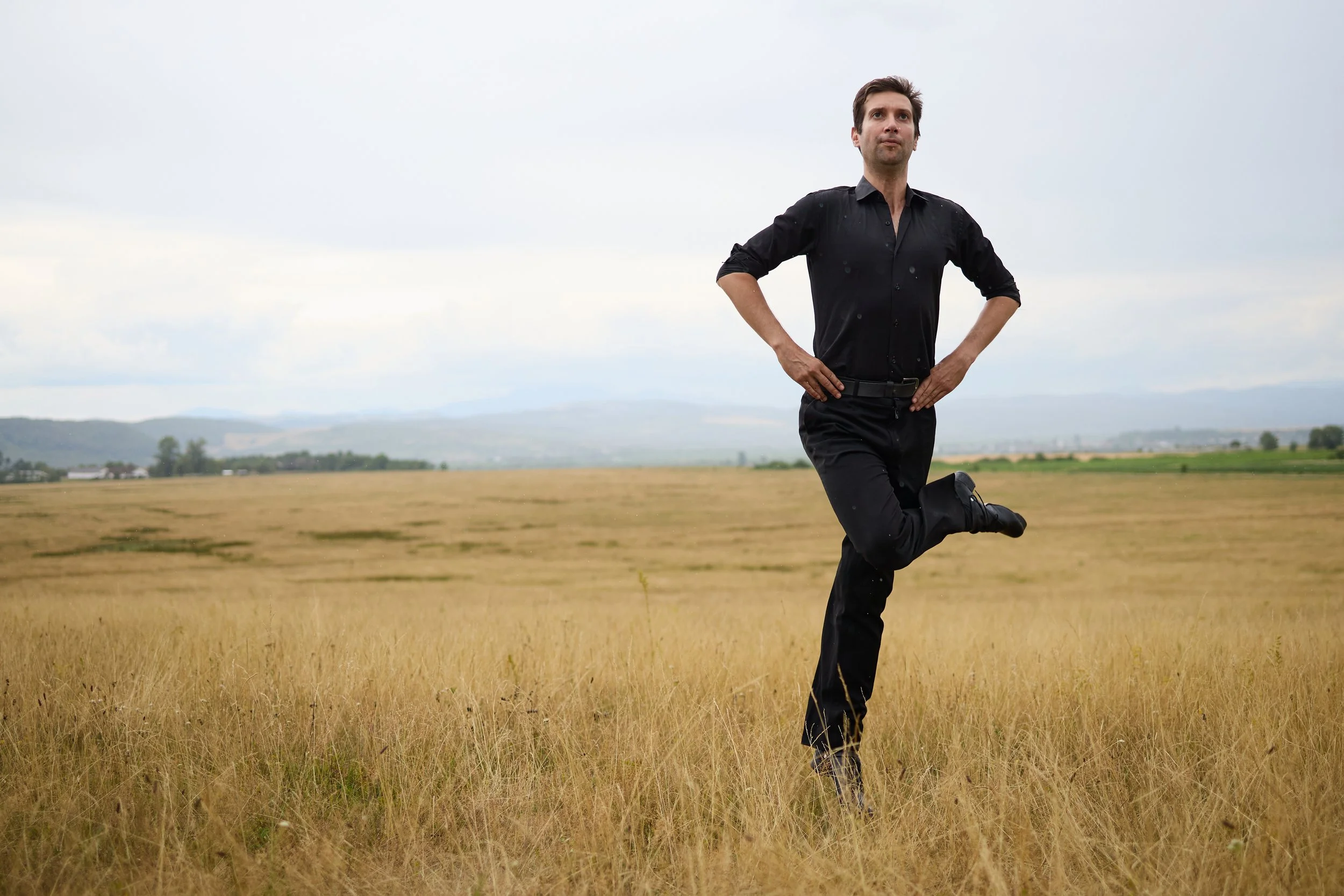 A man in a black shirt and pants running through a grassy field with a cloudy sky overhead.