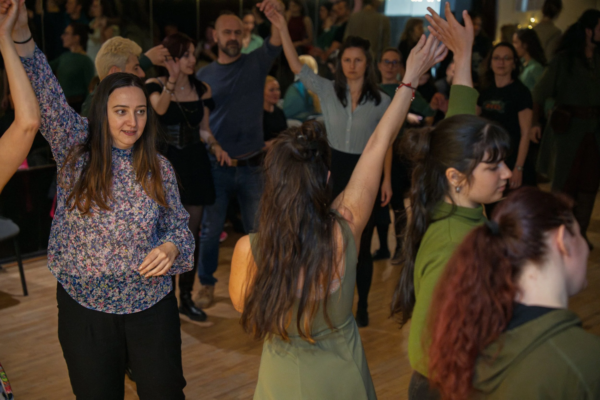 People dancing at a social event in a large room, with some holding hands and others raising their arms.